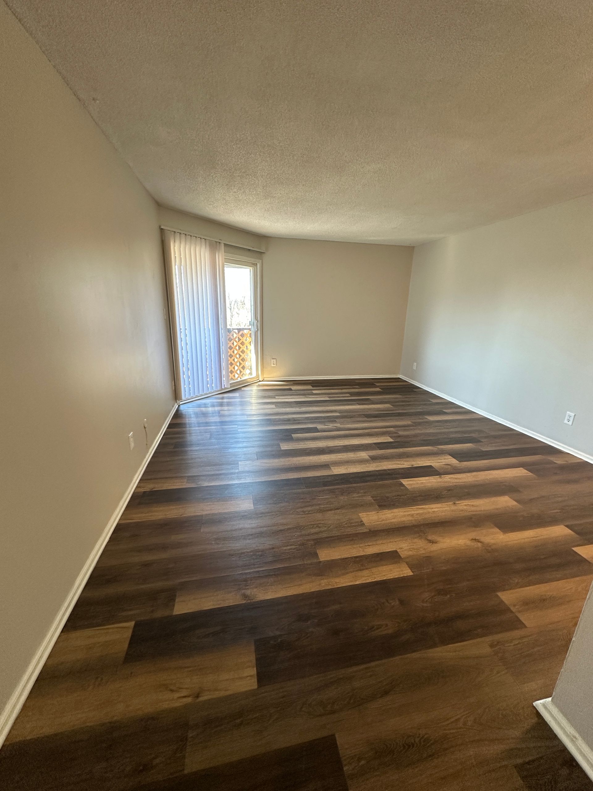 Empty room with wood-look flooring, light gray walls, and a door to a balcony.