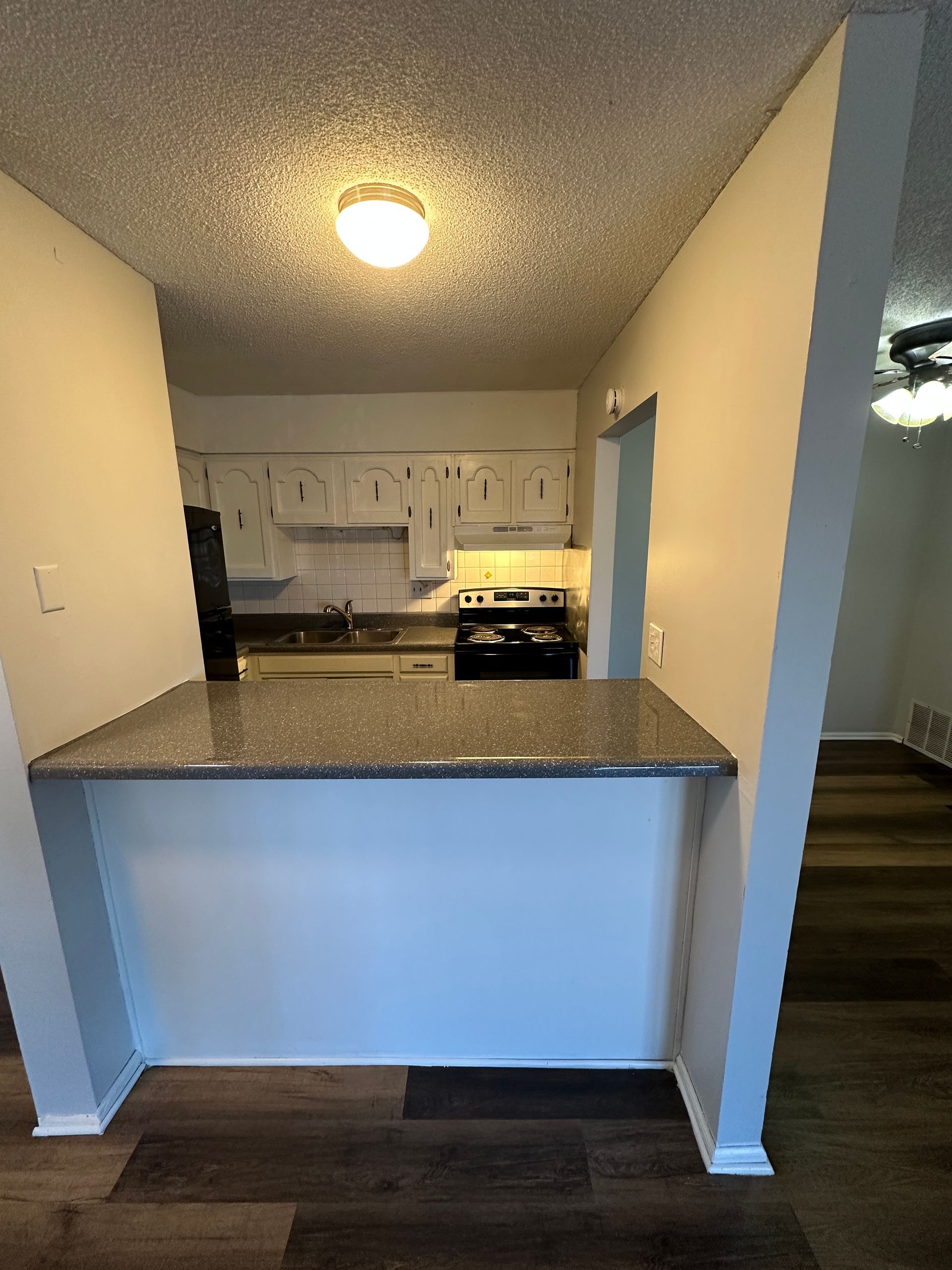 Kitchen with a breakfast bar, white cabinets, black appliances, and dark flooring.