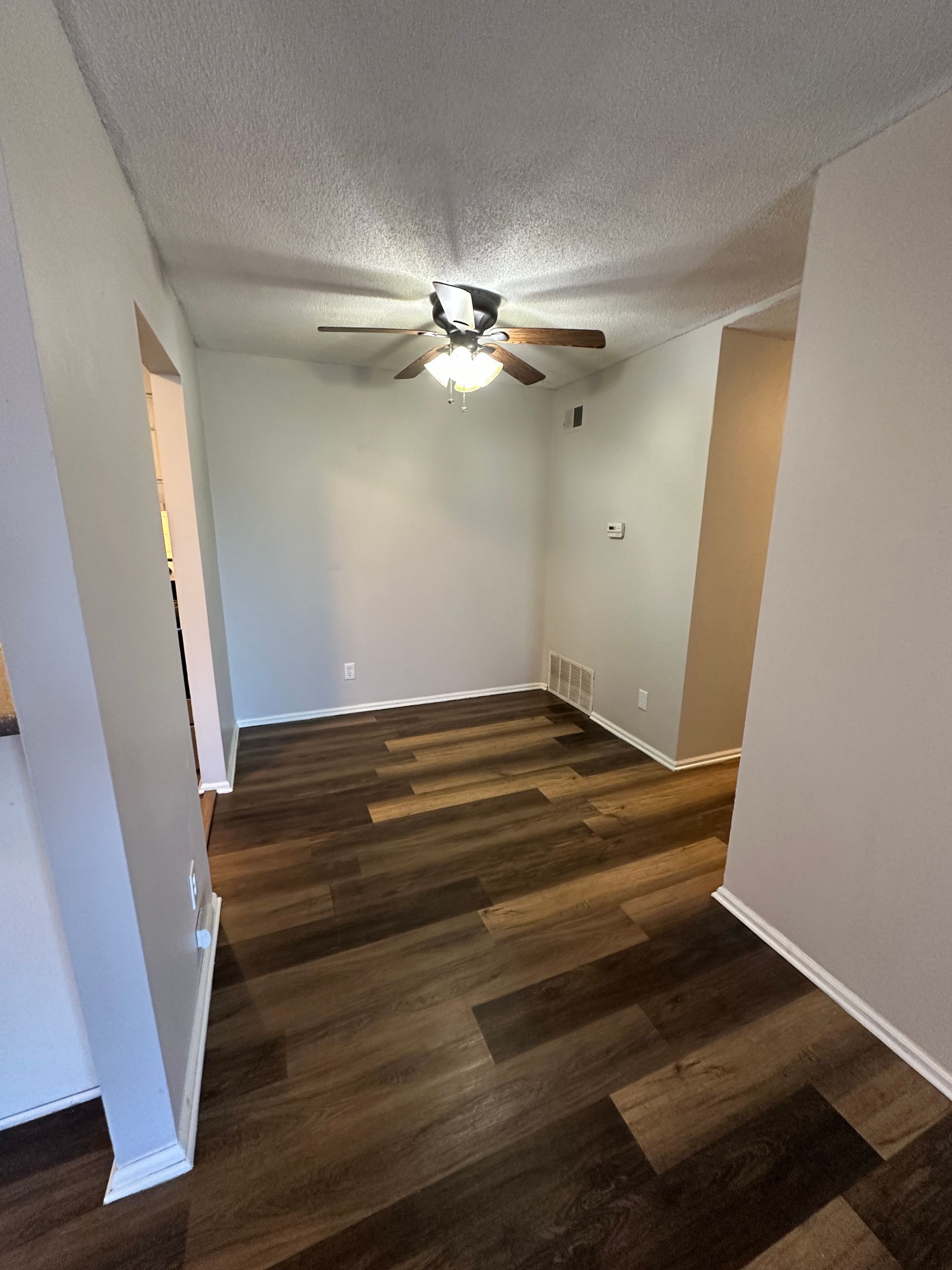 Empty room with wood-look flooring, light gray walls, and a ceiling fan.