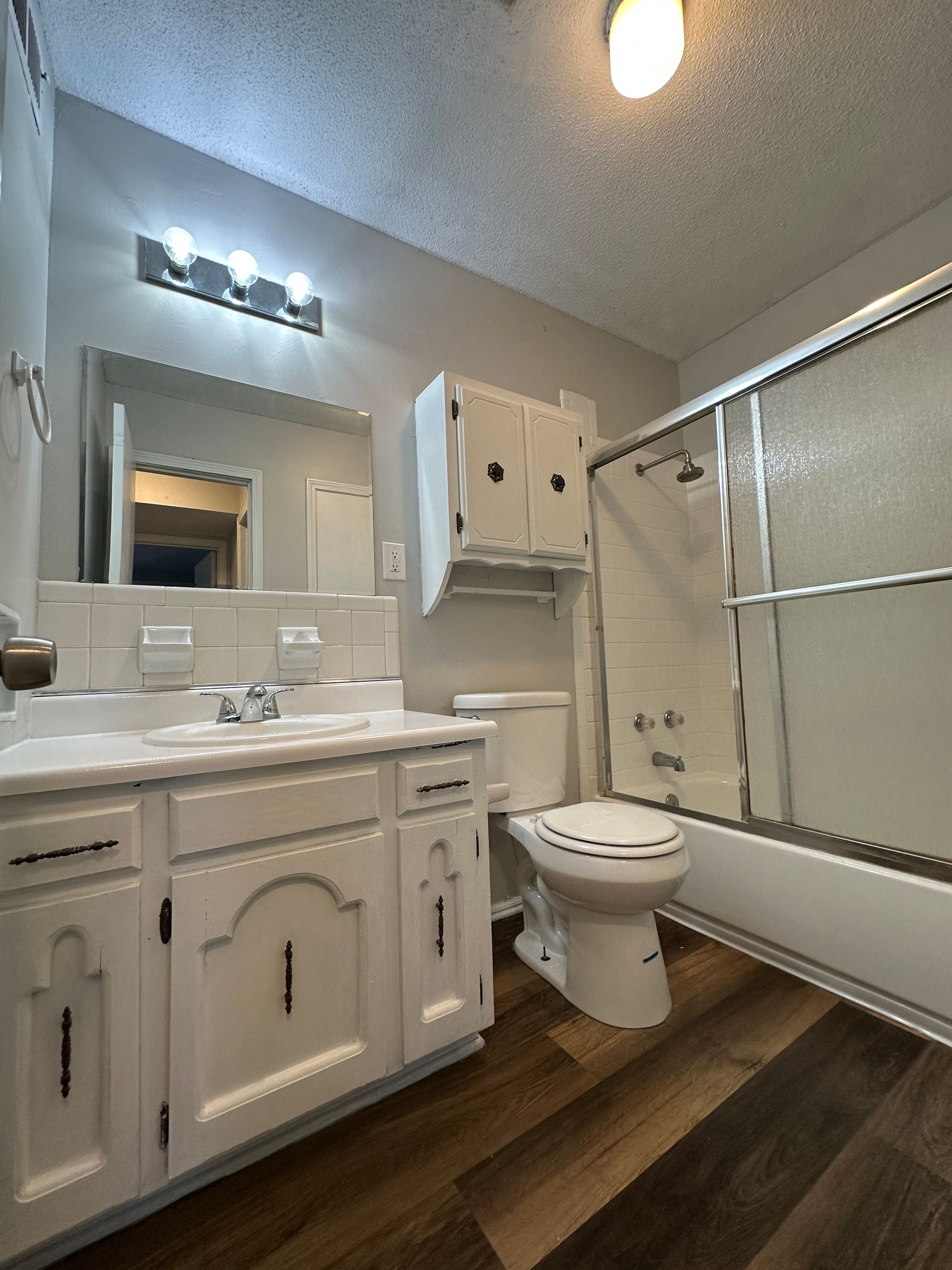 Bathroom with a white vanity, toilet, and shower. Dark brown floor, light gray walls.