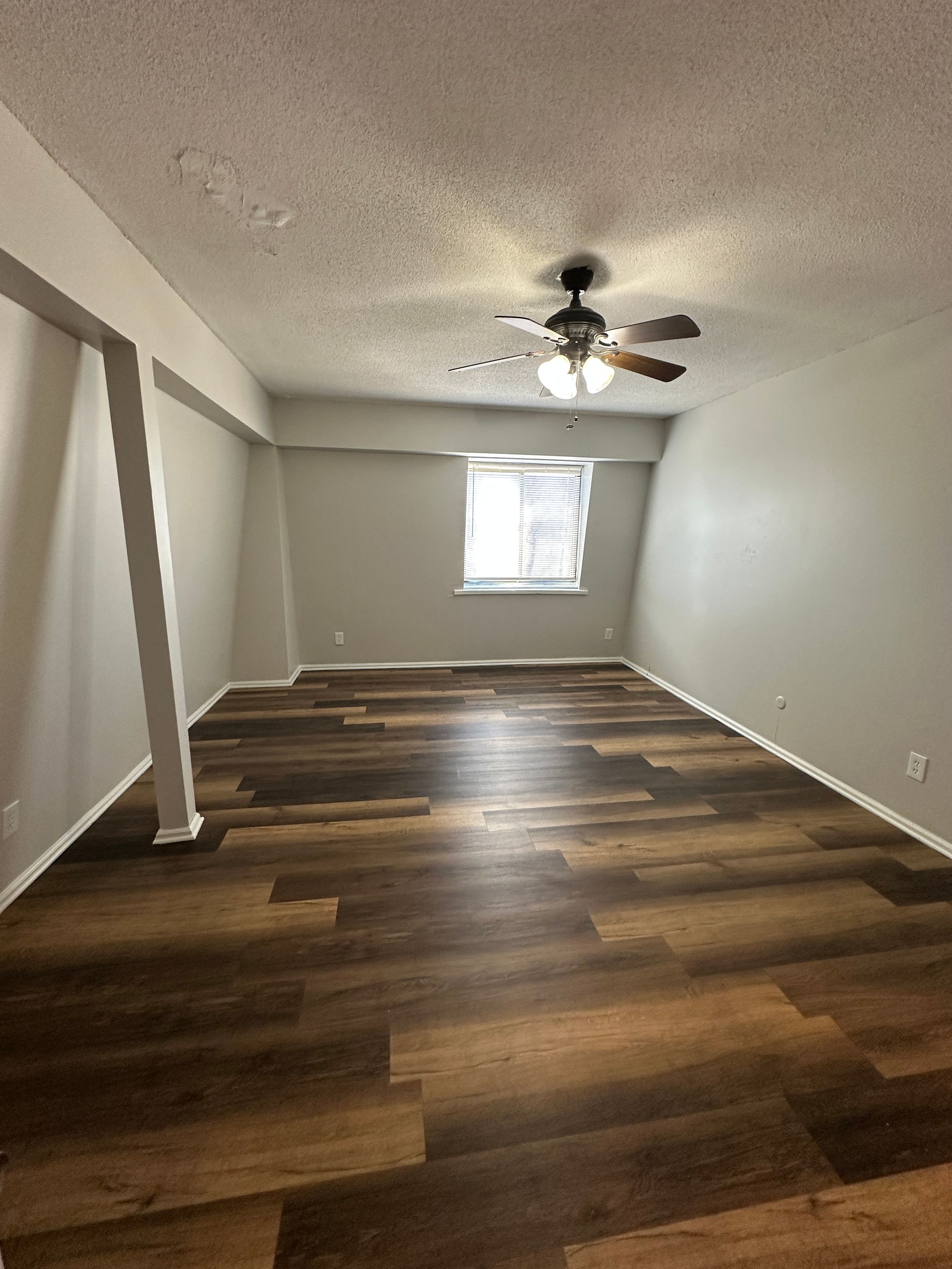 Empty room with wood-look floor, gray walls, ceiling fan, and window.