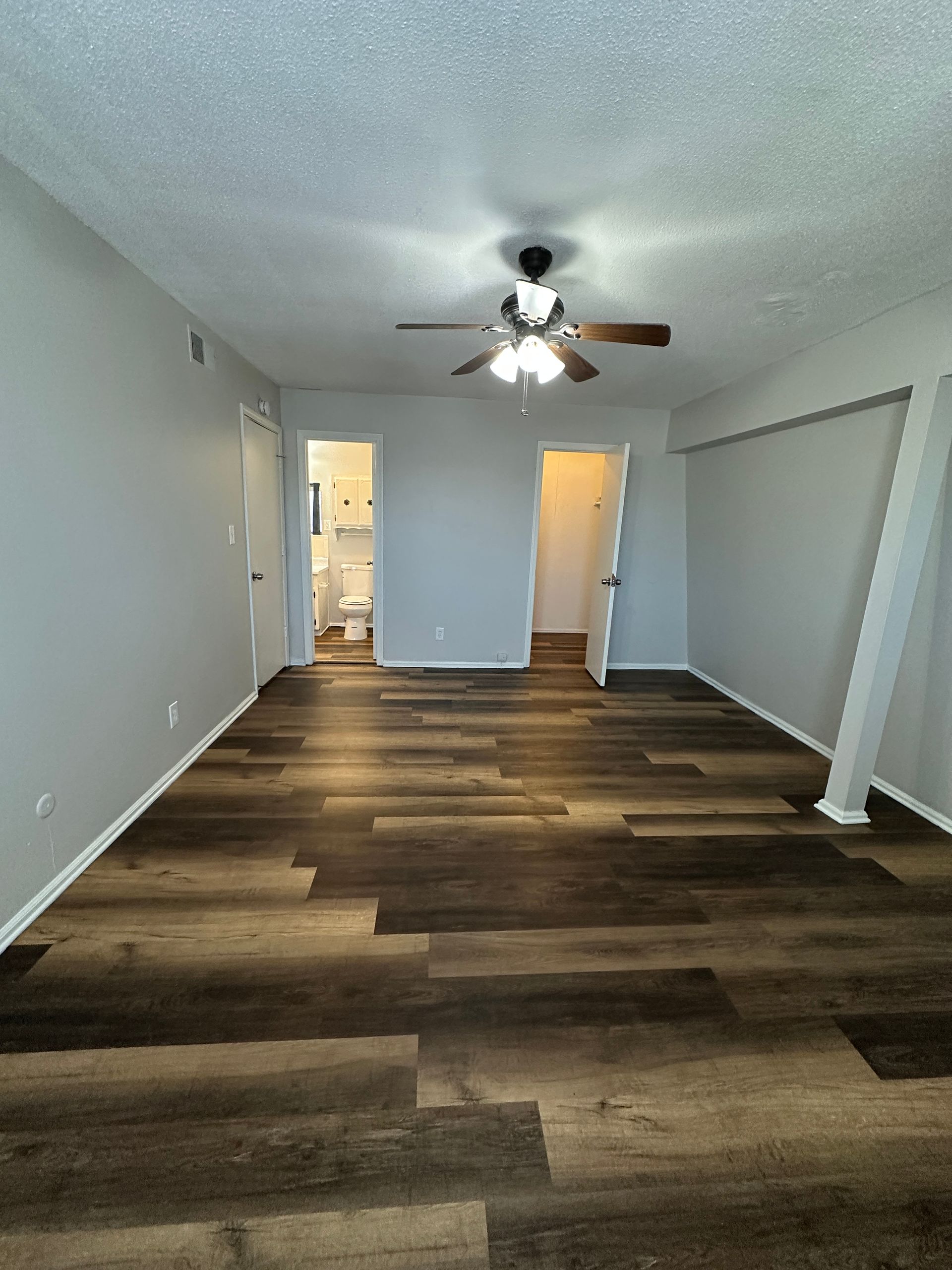Empty room with dark wood-look flooring, light gray walls, white trim, ceiling fan, and open doorways.