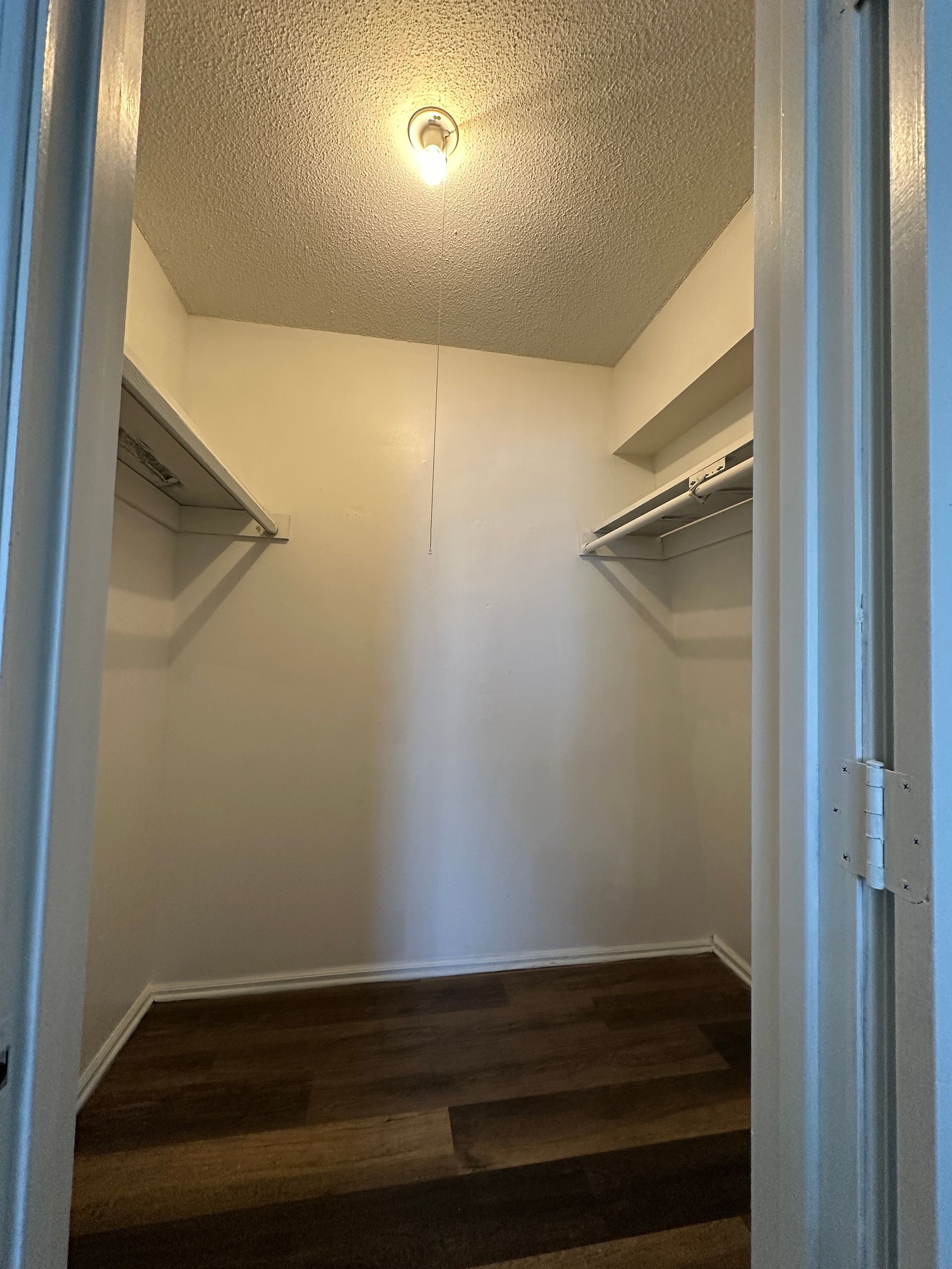 Empty walk-in closet with shelves and wood-look flooring, viewed from the doorway.