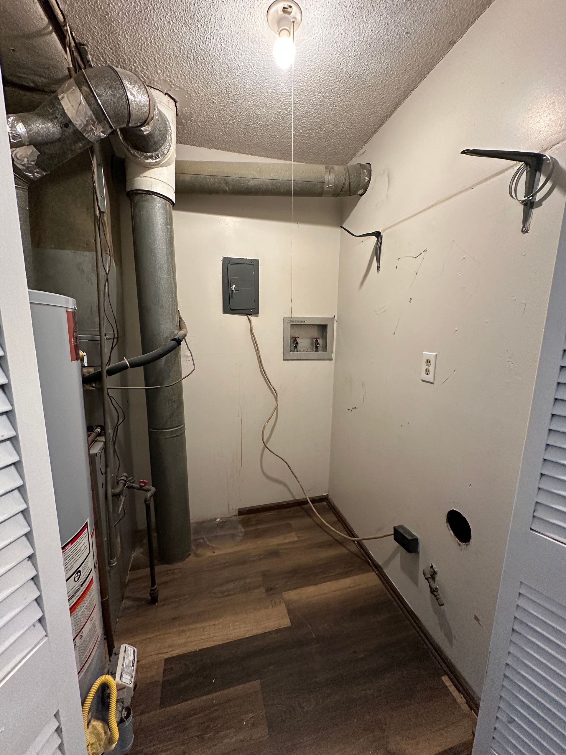 Laundry room with water heater, electrical panel, and clothesline. Wooden floor and white walls.