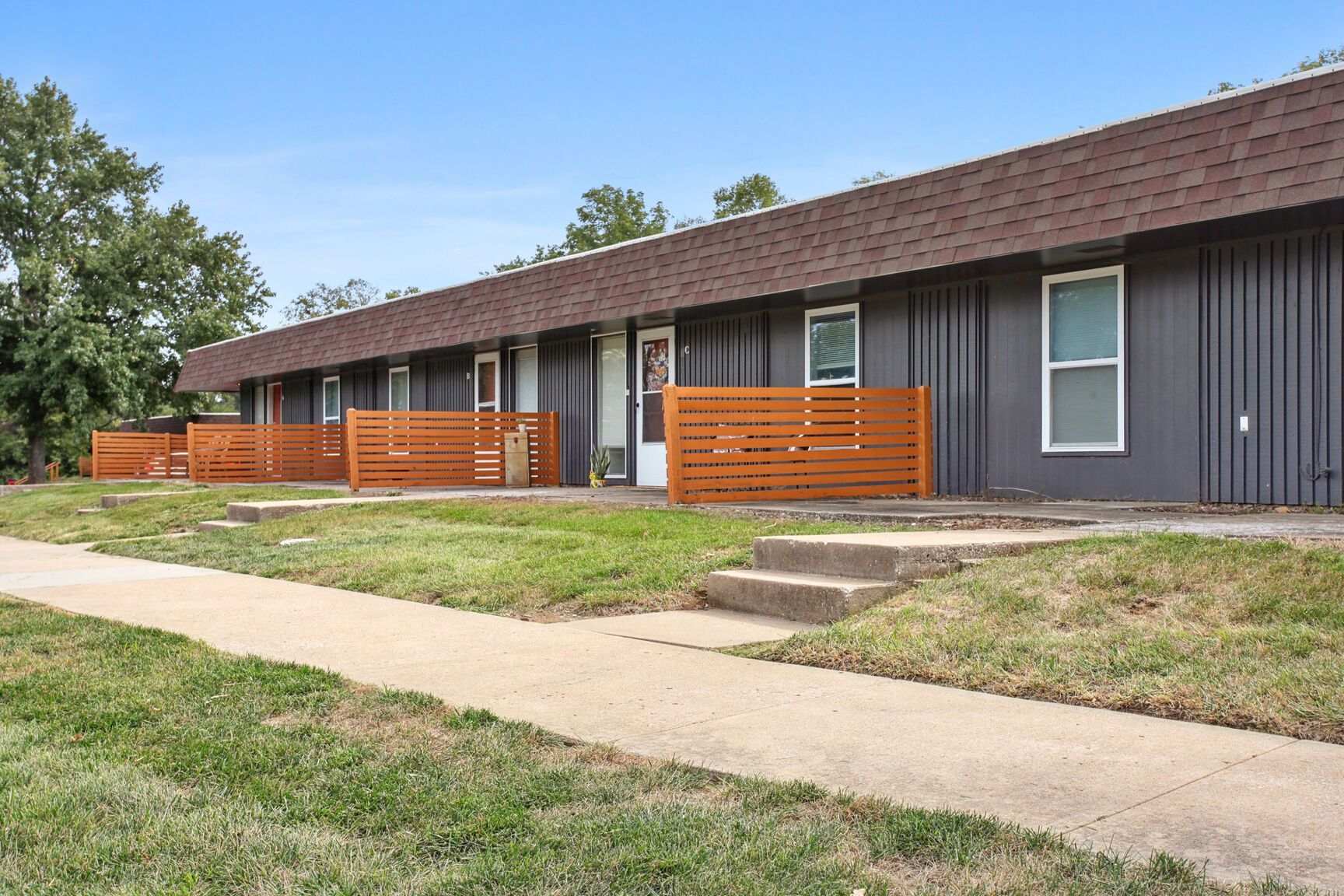 Row of gray townhouses with brown roofs and wooden fences.