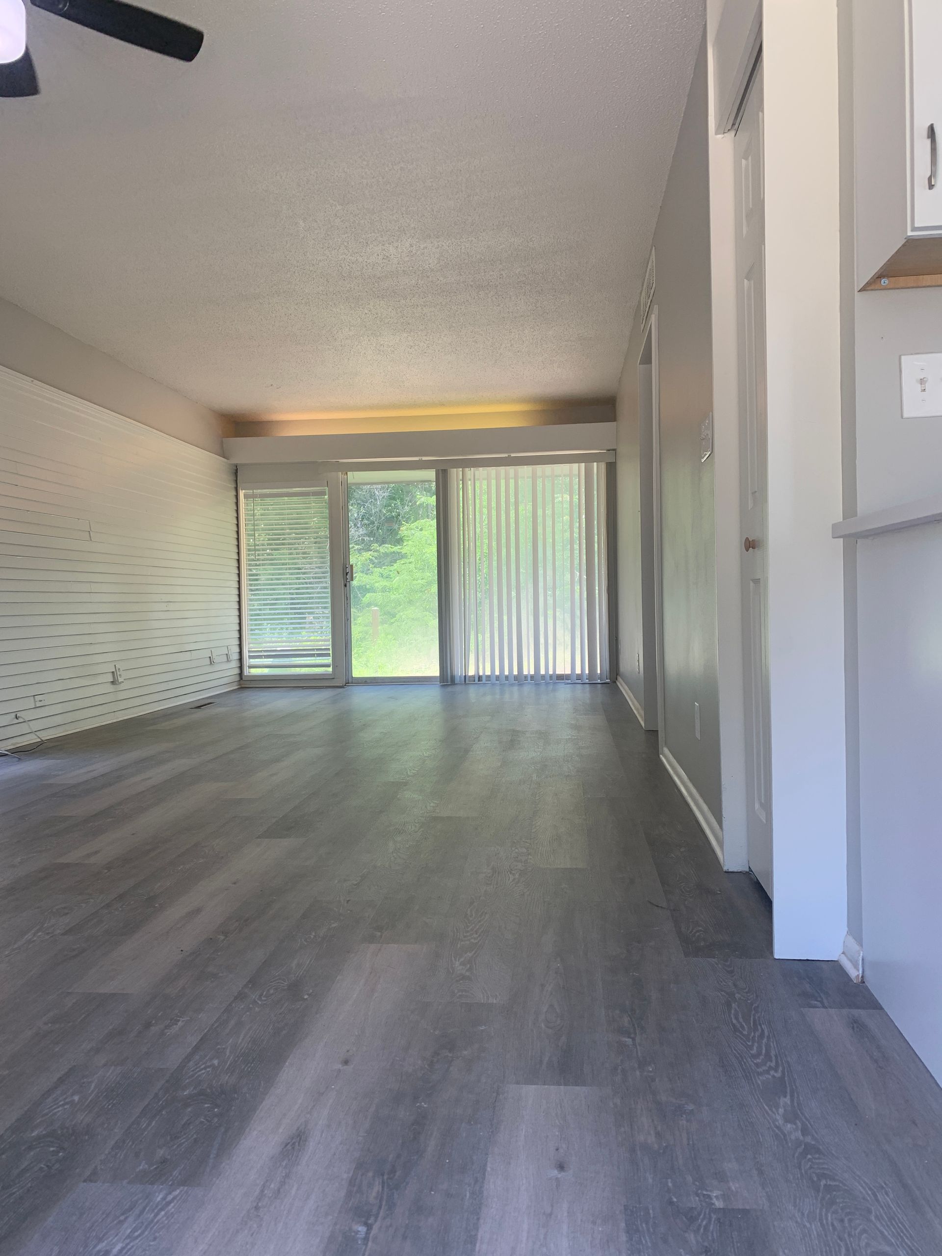 Empty room with gray flooring, sliding glass doors, white walls, and a ceiling fan.