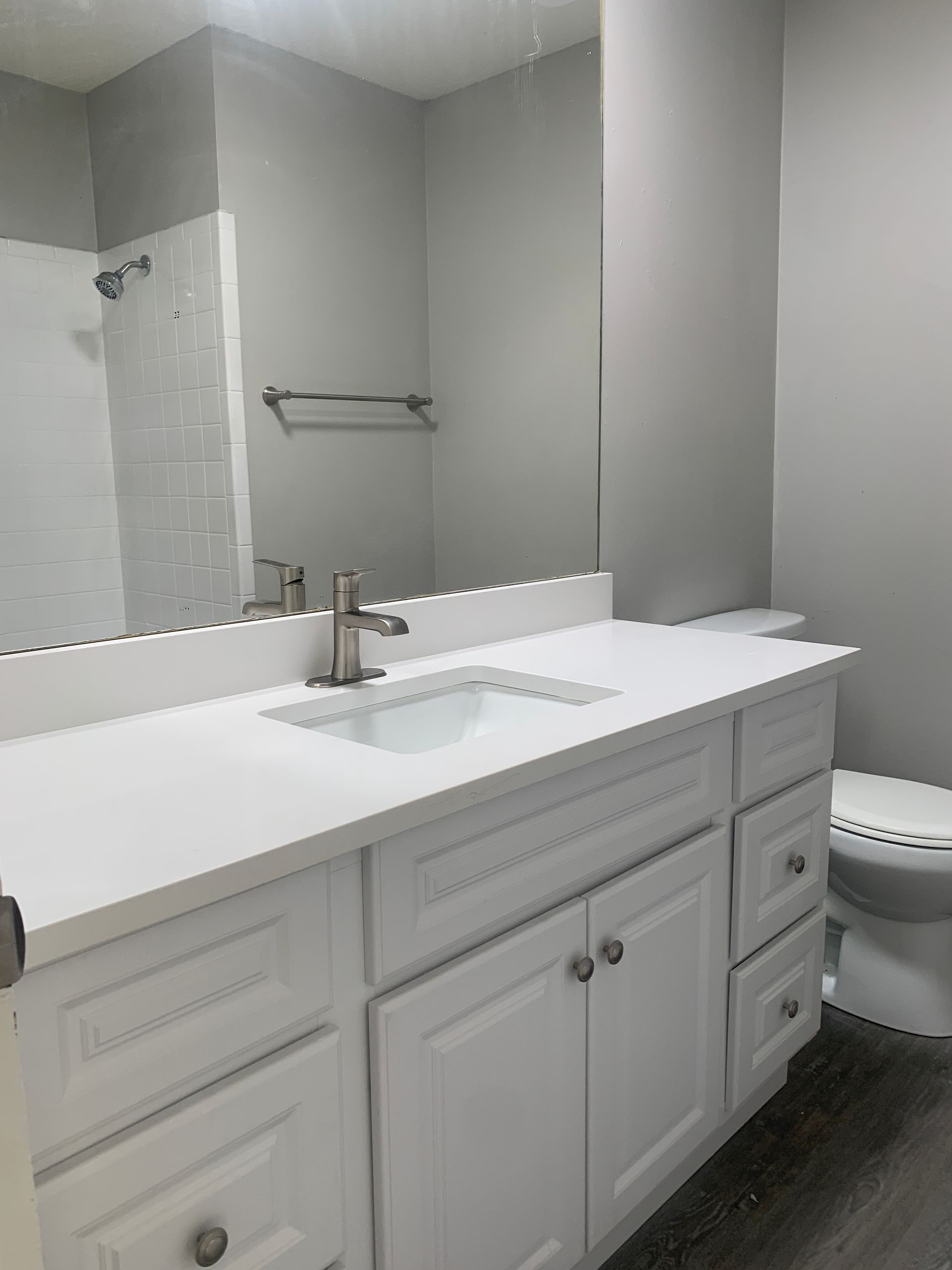 White bathroom vanity with sink and mirror, gray walls, and a toilet.