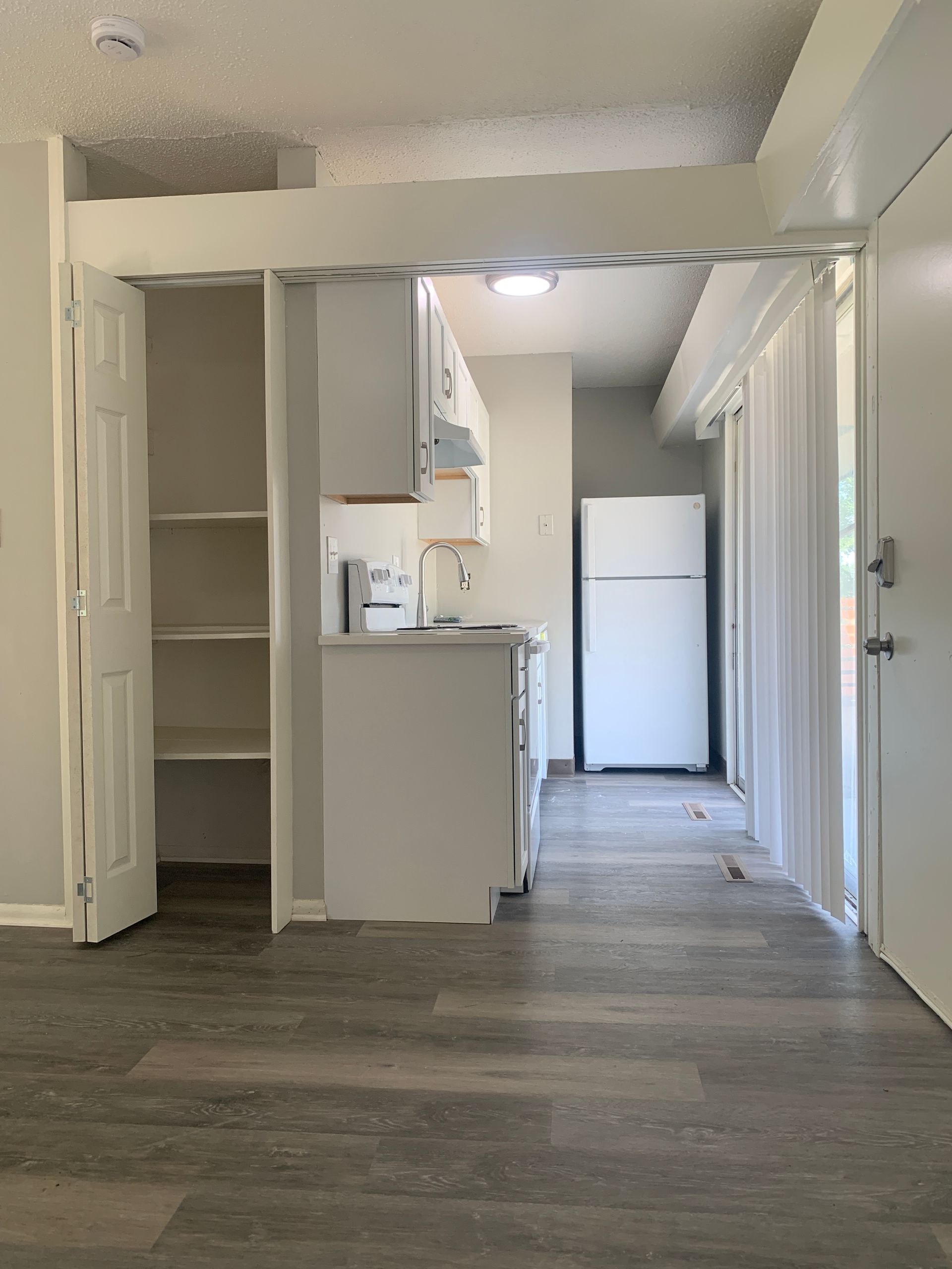 Interior shot of an apartment kitchen area with white cabinets and fridge, wooden floor.