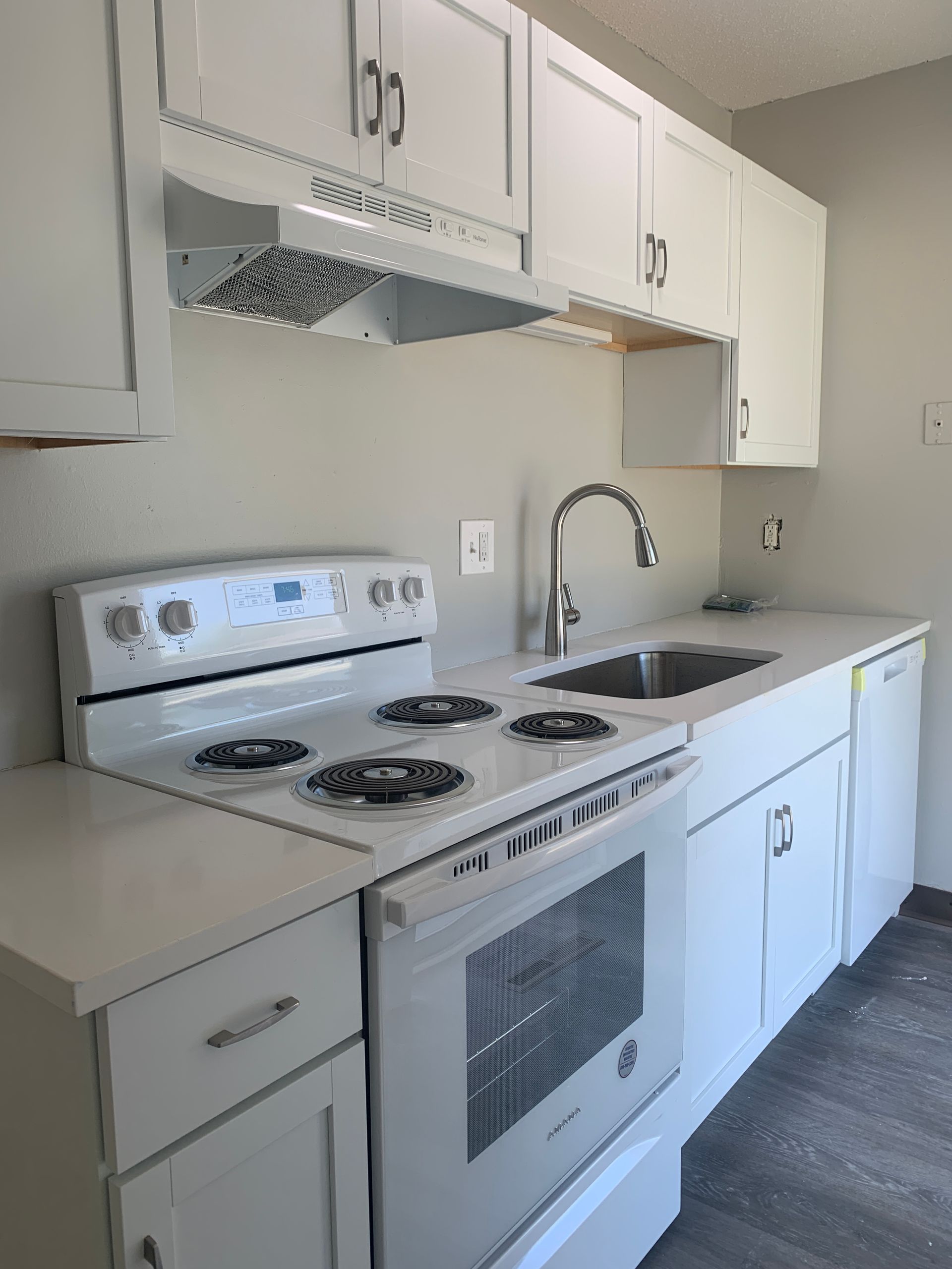 White kitchen with cabinets, stove, sink, and range hood.