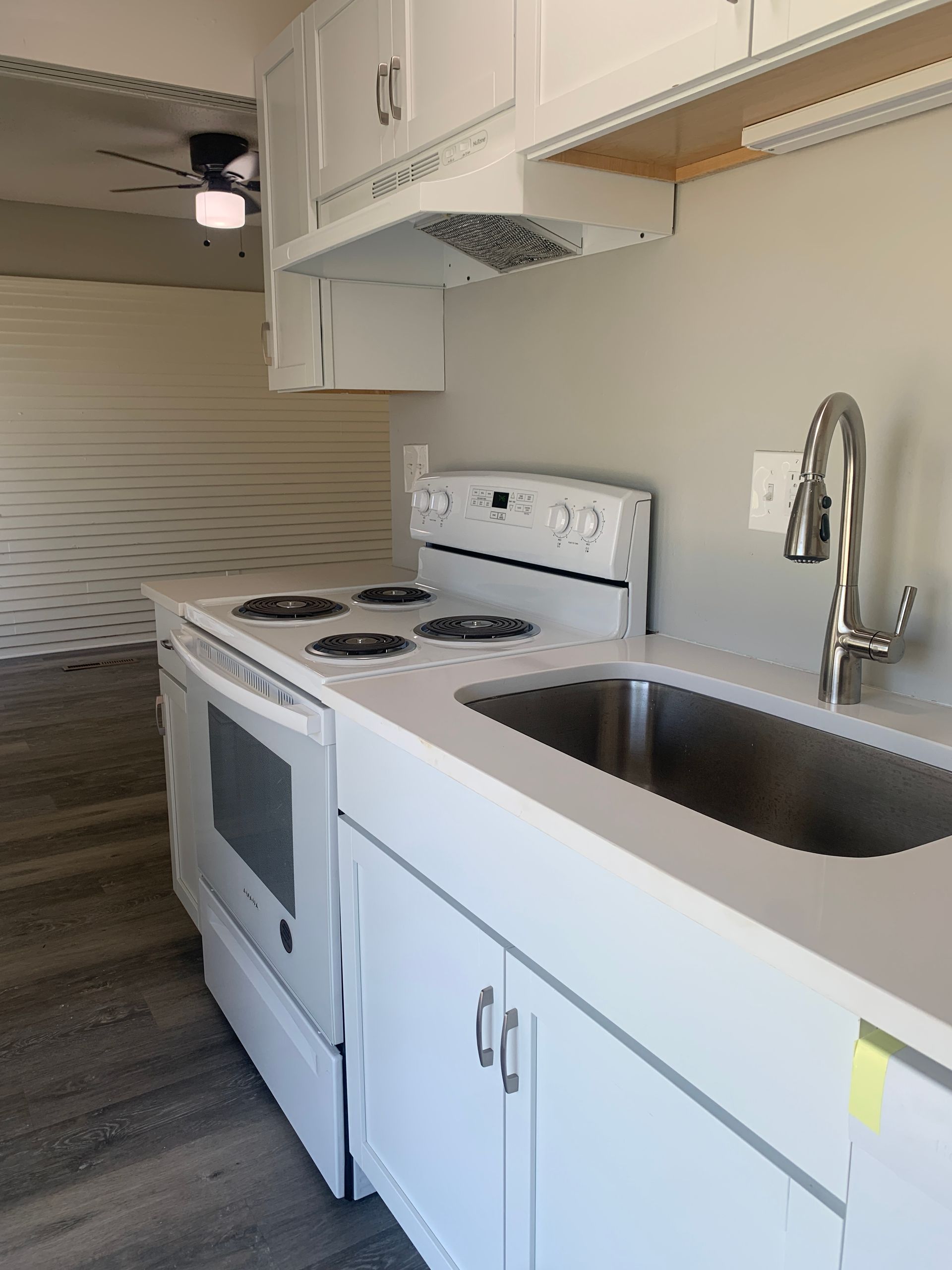 White kitchen with stove, sink, cabinets, and a ceiling fan.