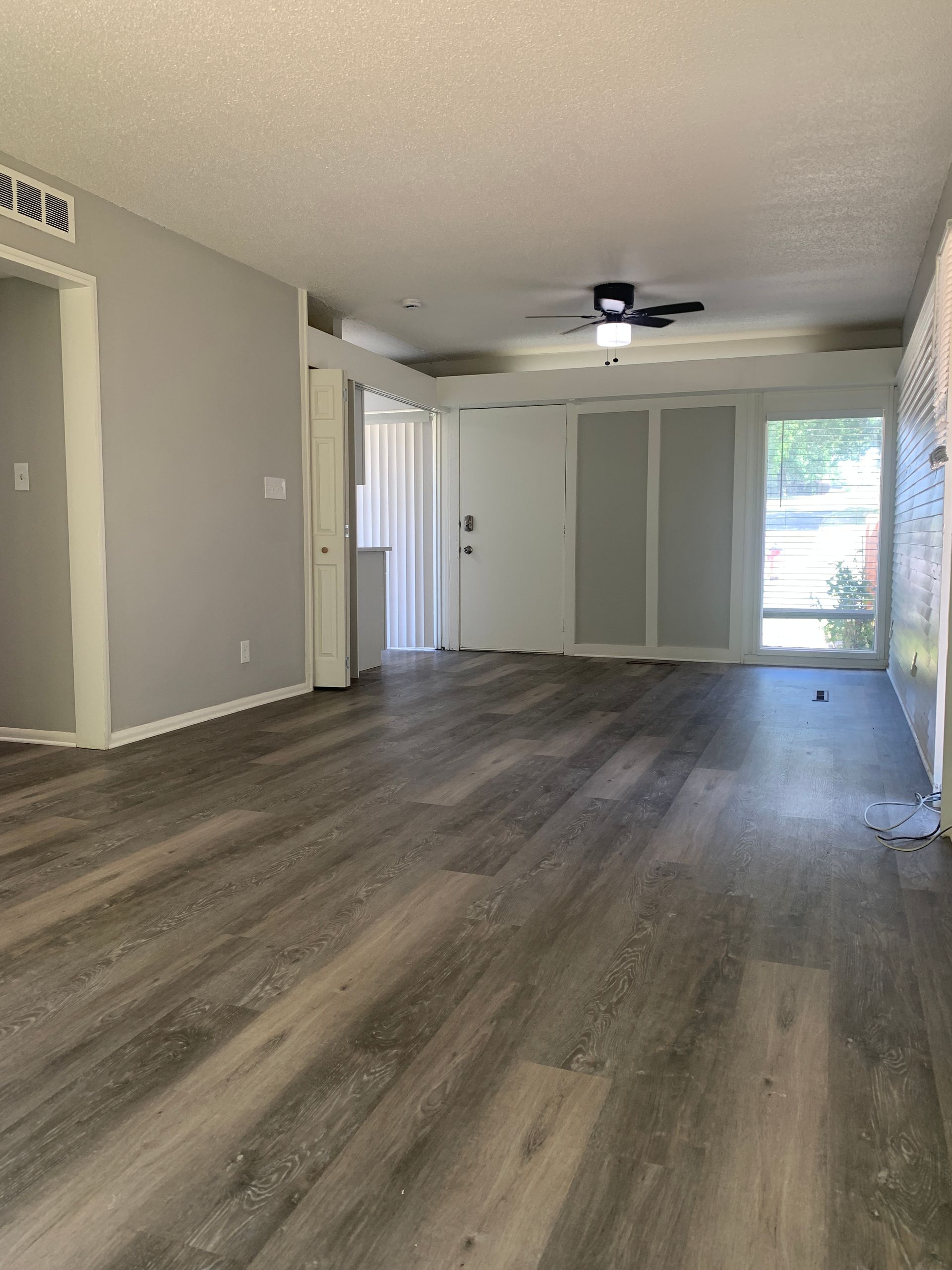 Empty living room with wood-look flooring, gray walls, and white trim.  A door and a window are visible.
