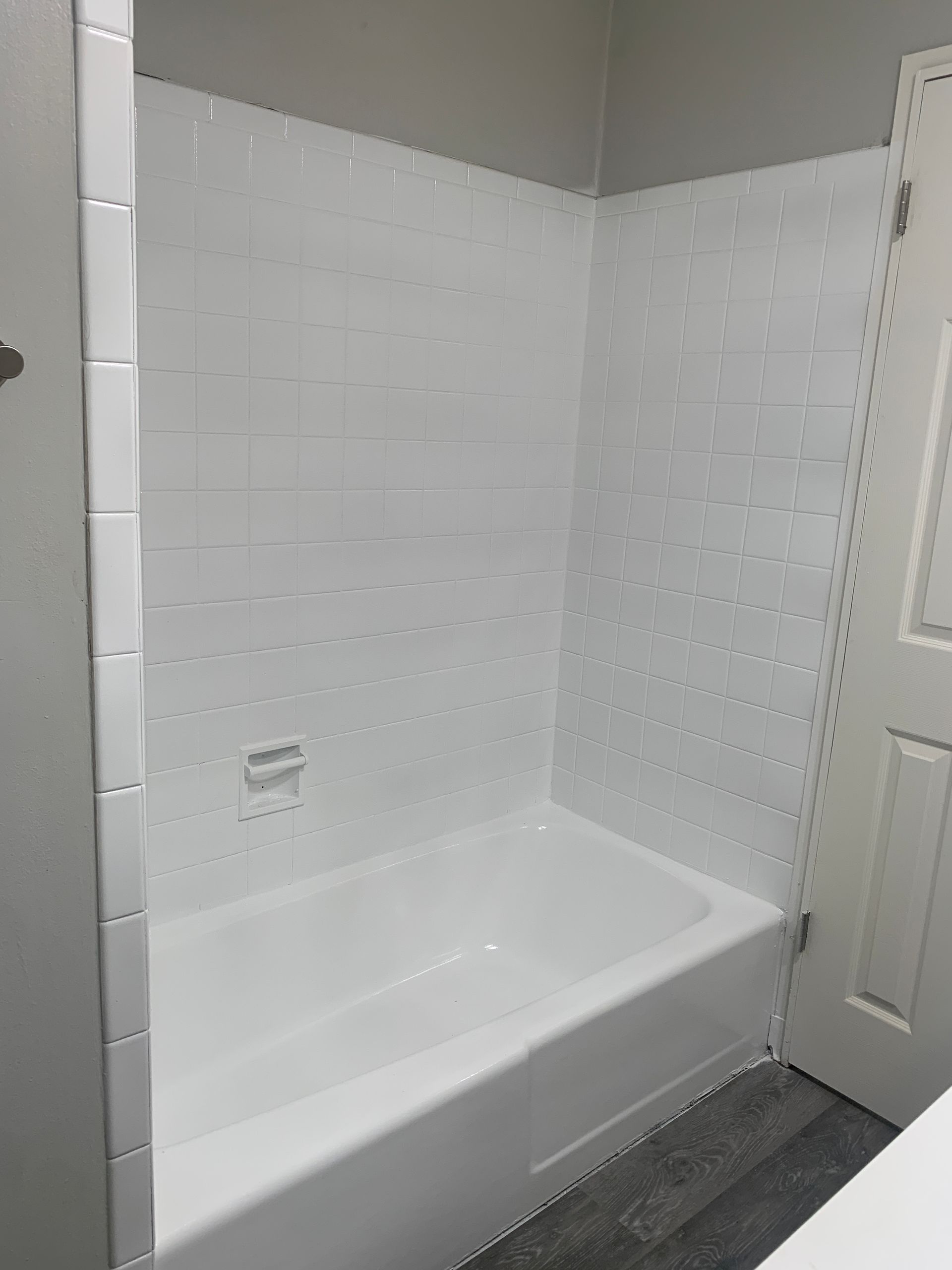 White bathroom with a tub and tiled walls, next to a white door.