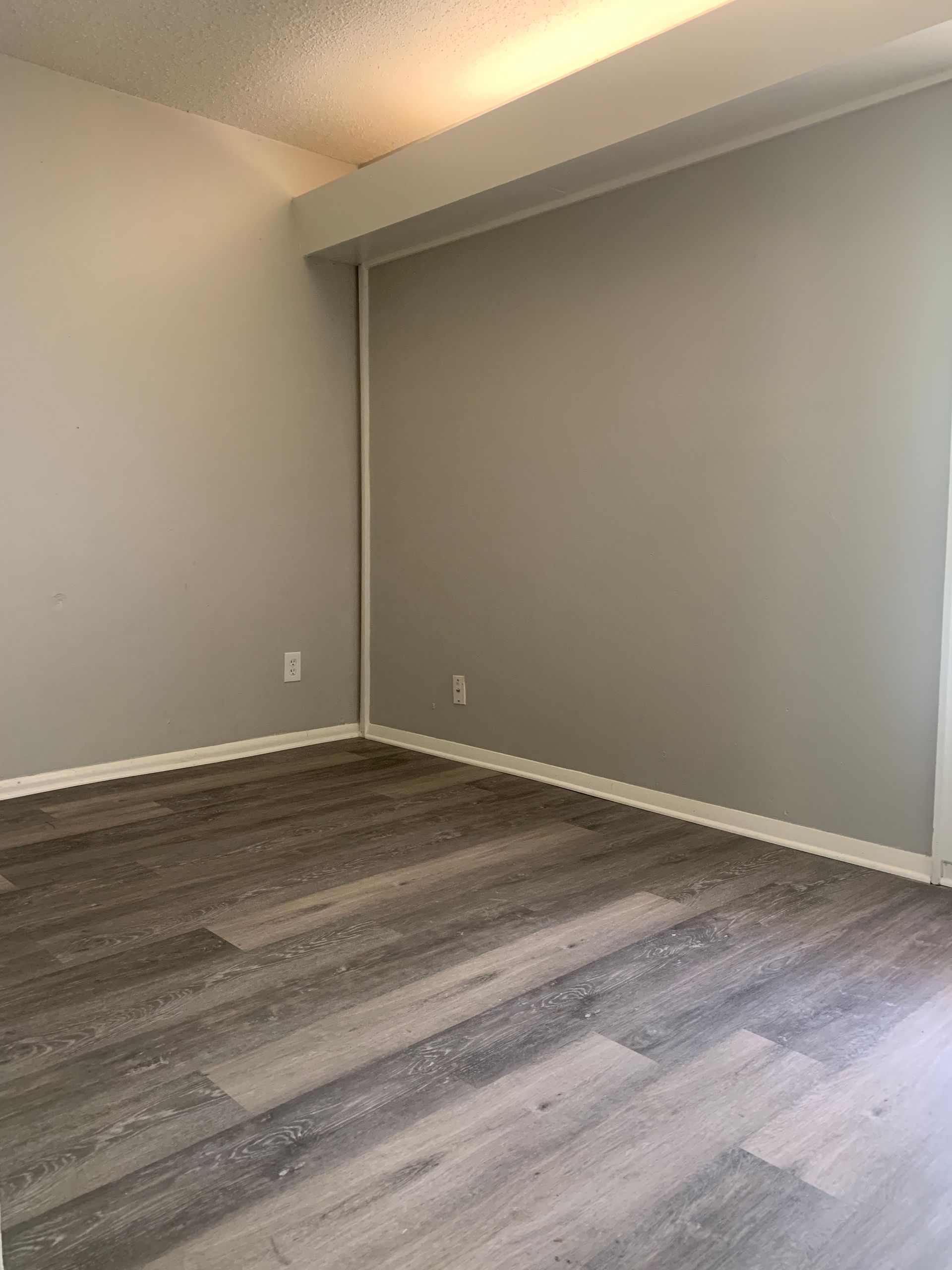 Empty room with gray walls, wood-look flooring, and a white ceiling beam.