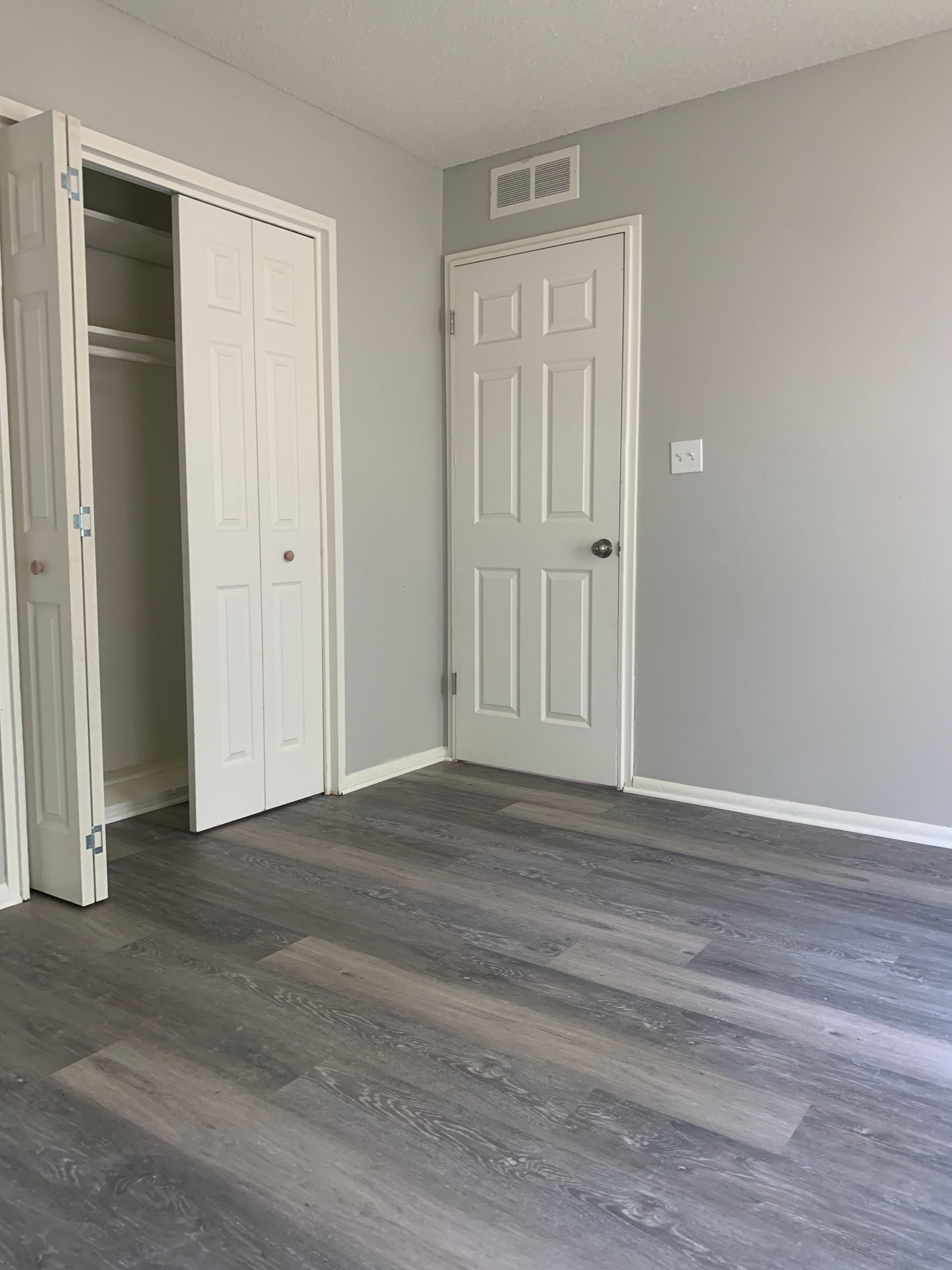 Bedroom with gray walls, white doors, and gray wood-look flooring. Closet with open doors on the left.