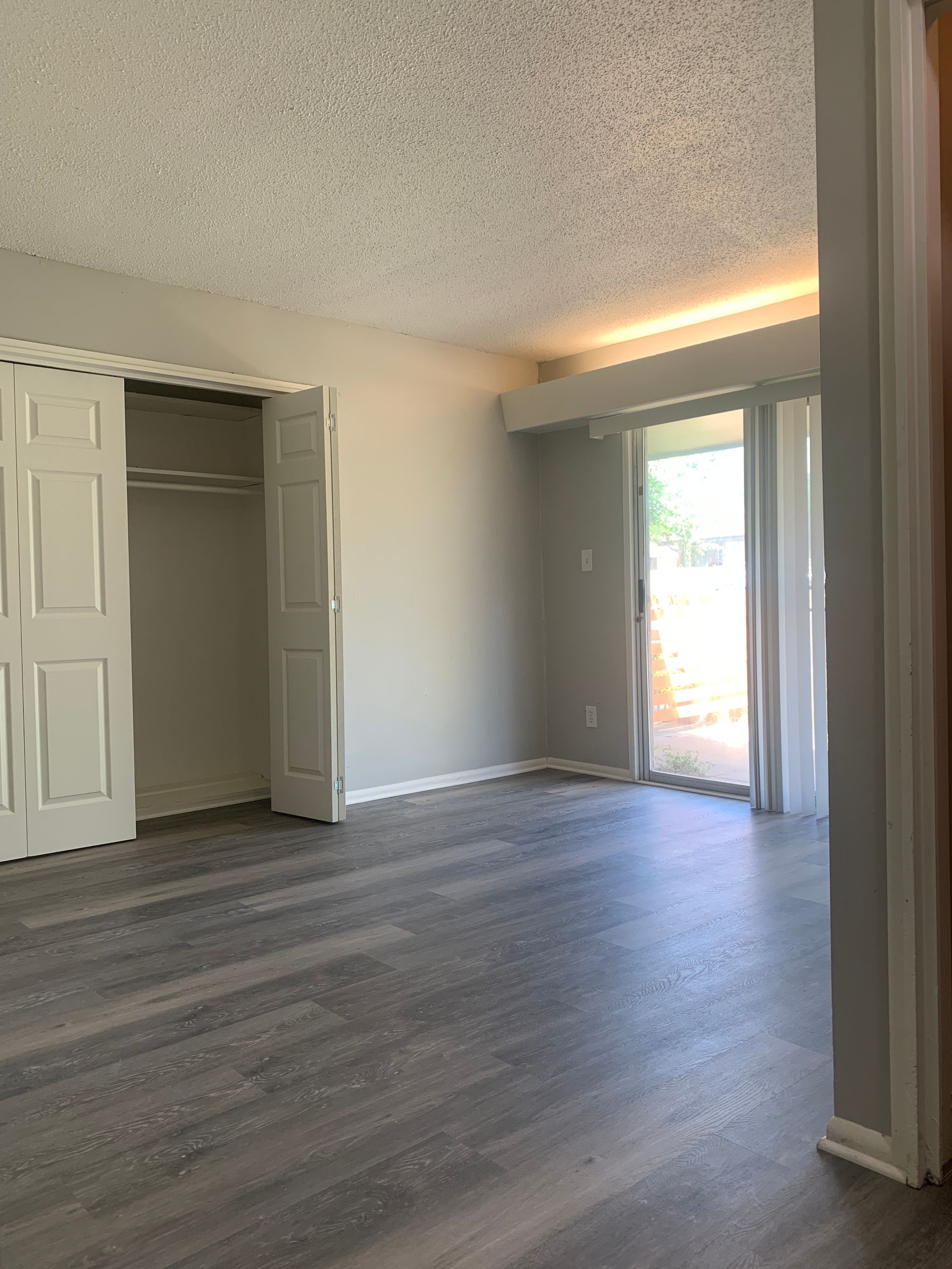 An empty bedroom with gray laminate flooring, a closet, a sliding glass door, and a textured white ceiling.