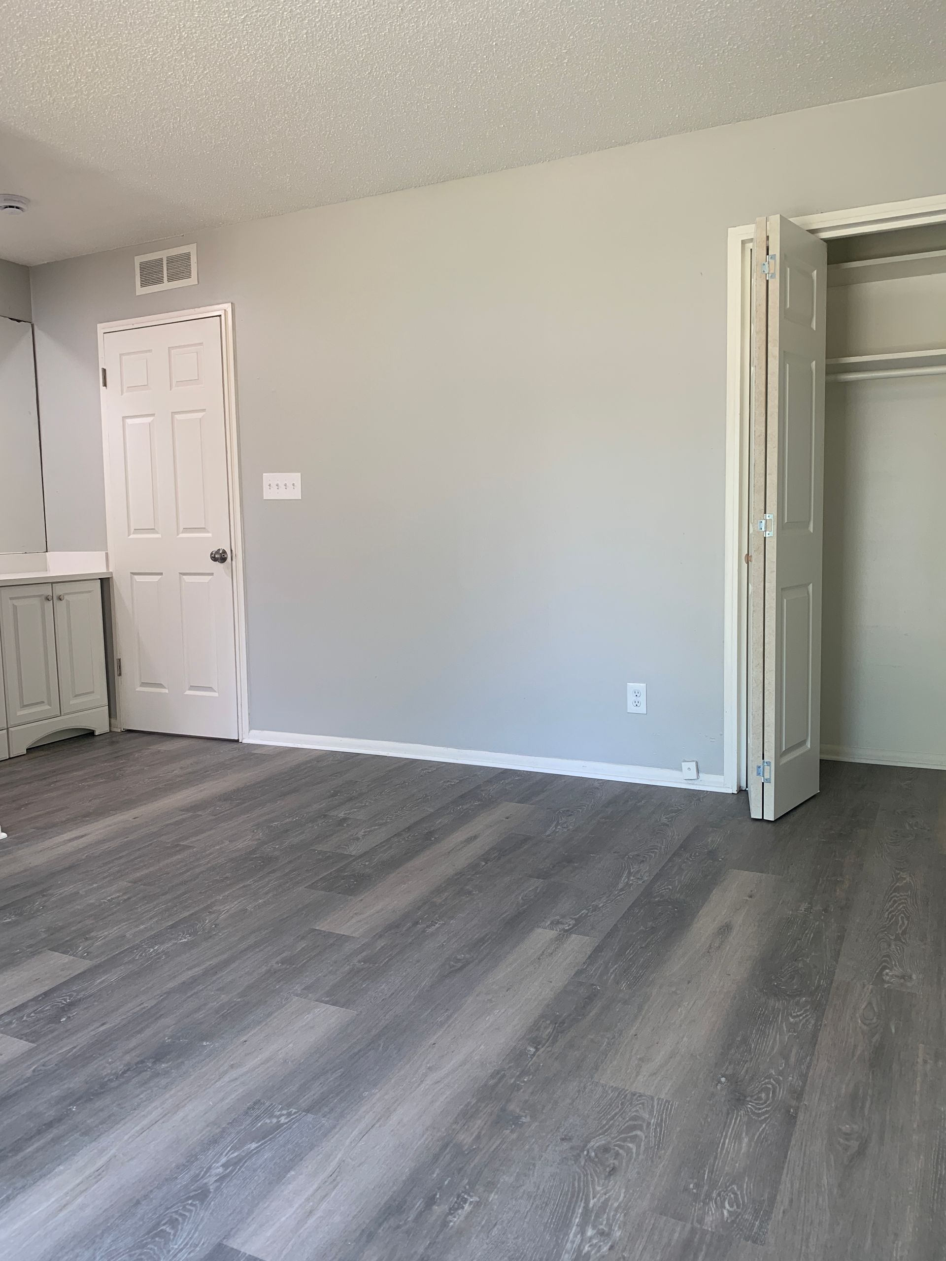 Empty room with gray walls, white trim, wood-look floor, and a closet.