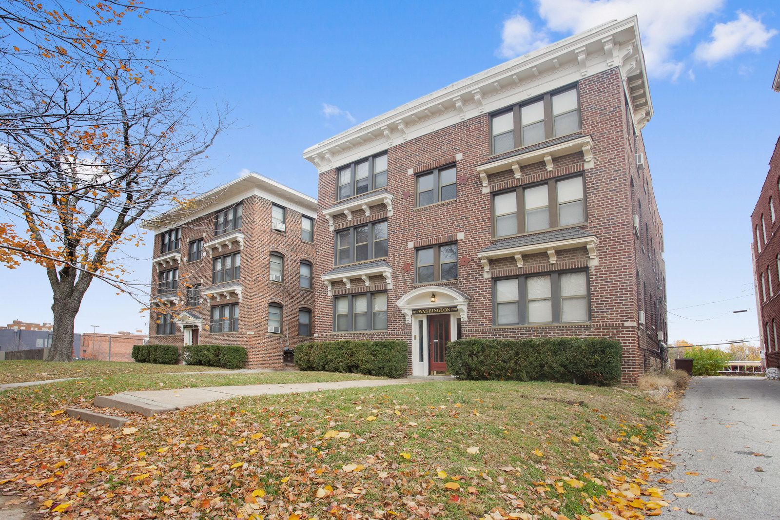 Brick apartment buildings with a green lawn and autumn leaves under a blue sky.