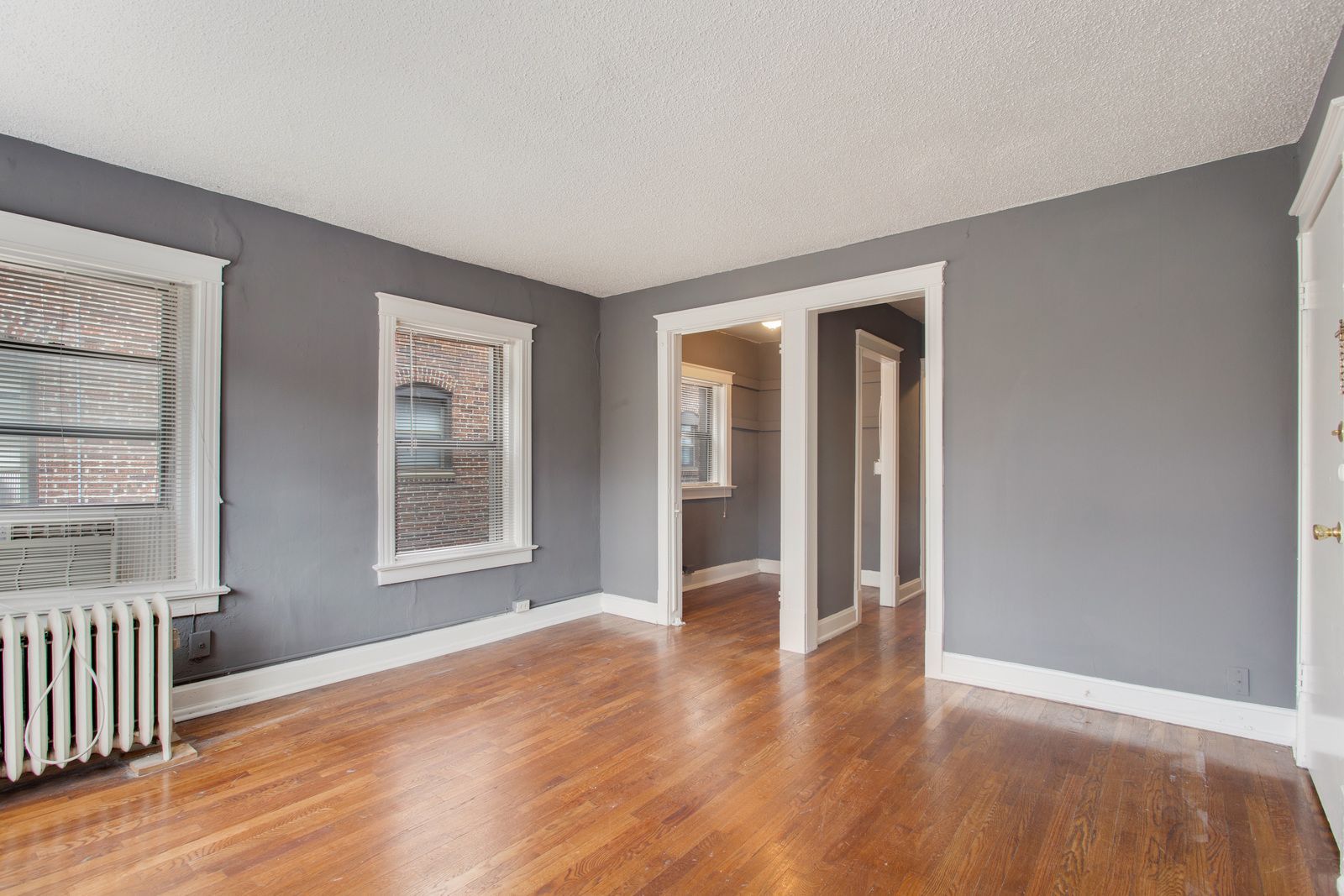 Empty room with gray walls, wood floor, white trim, and two windows.