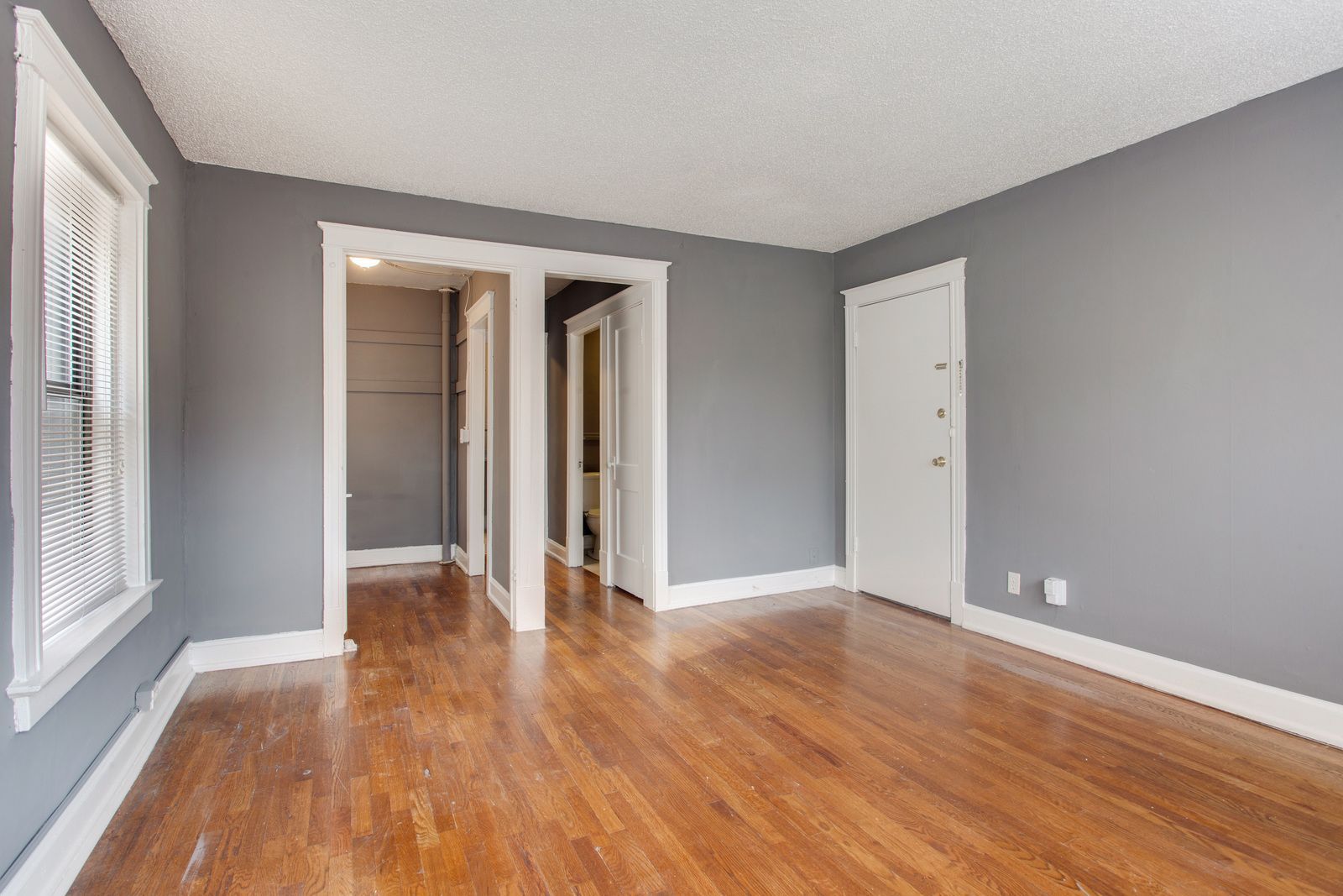 Empty room with gray walls, wood floor, white trim and door.