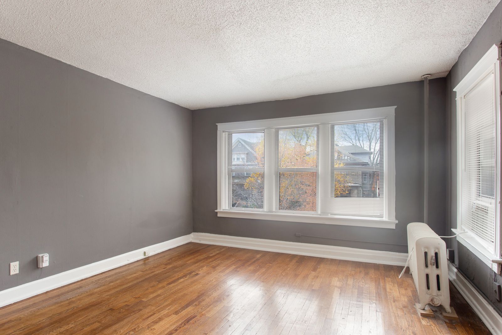 Empty room with gray walls, hardwood floor, white trim, and a window.