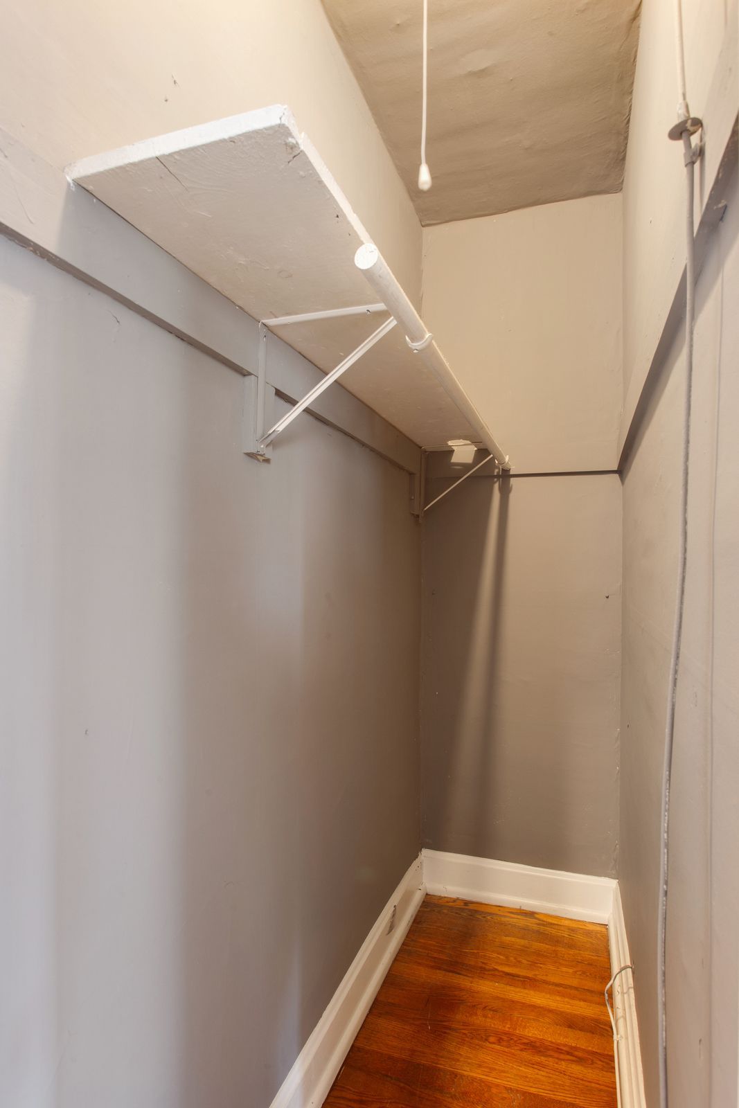 An empty closet with a shelf and a hanging rod, painted gray, and a wood floor.