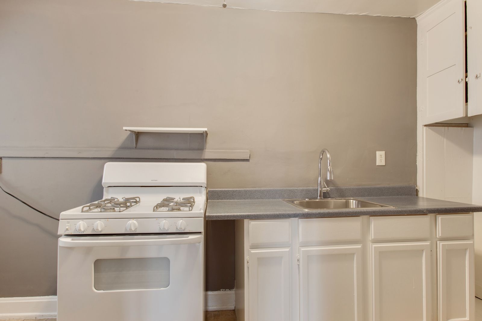 Kitchen with white stove and cabinets, gray countertop and wall, and a stainless steel sink.