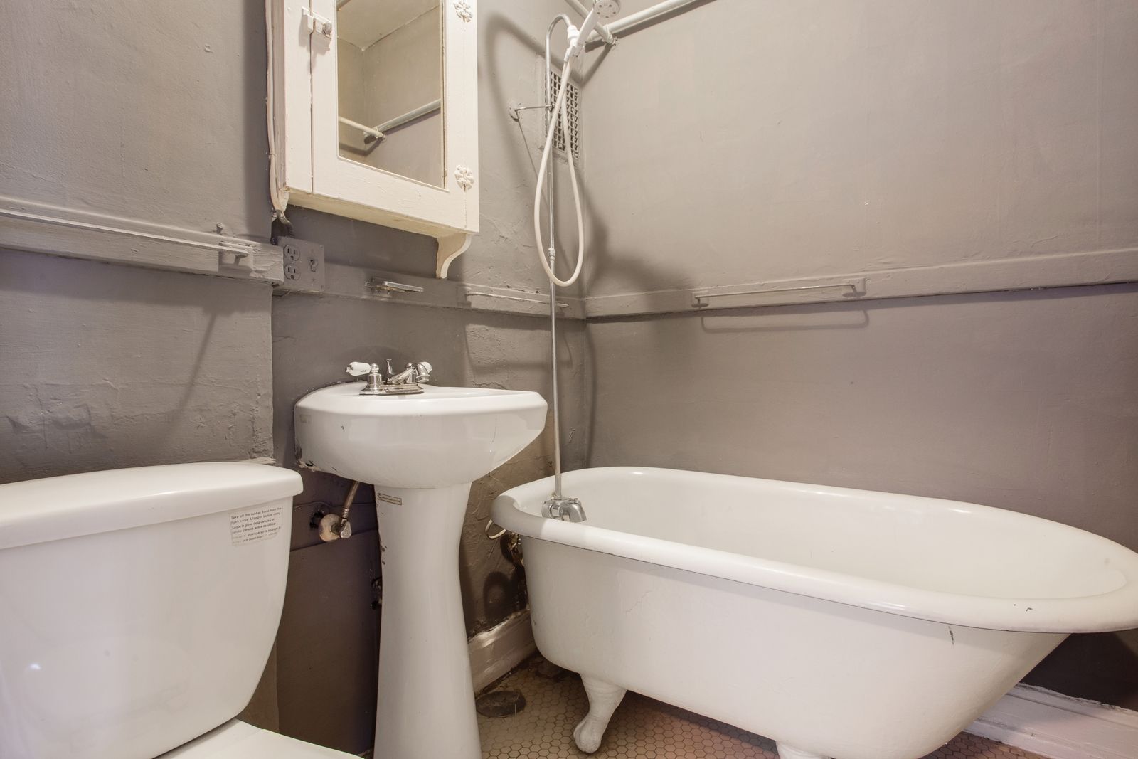 Small bathroom with a white pedestal sink, toilet, and clawfoot tub, gray walls.