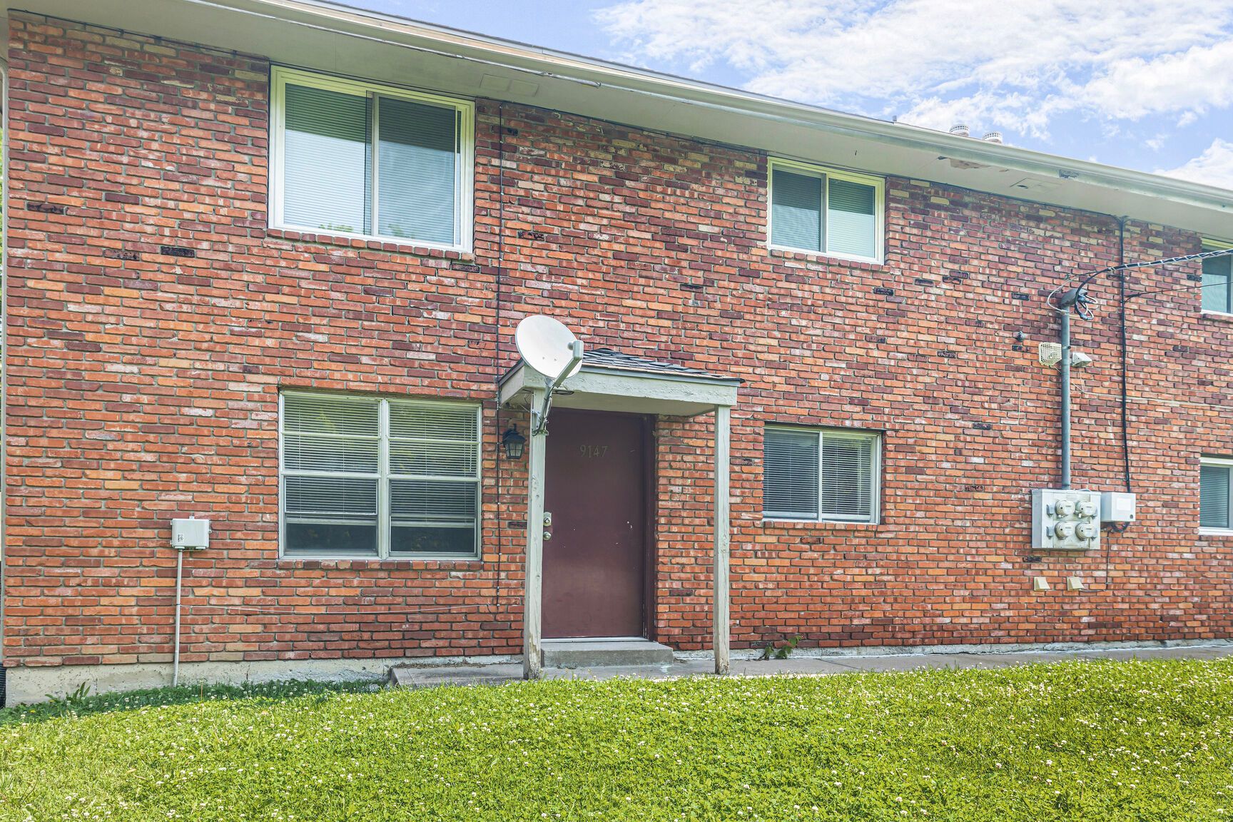 Red brick apartment building with a brown door, windows, and a satellite dish.