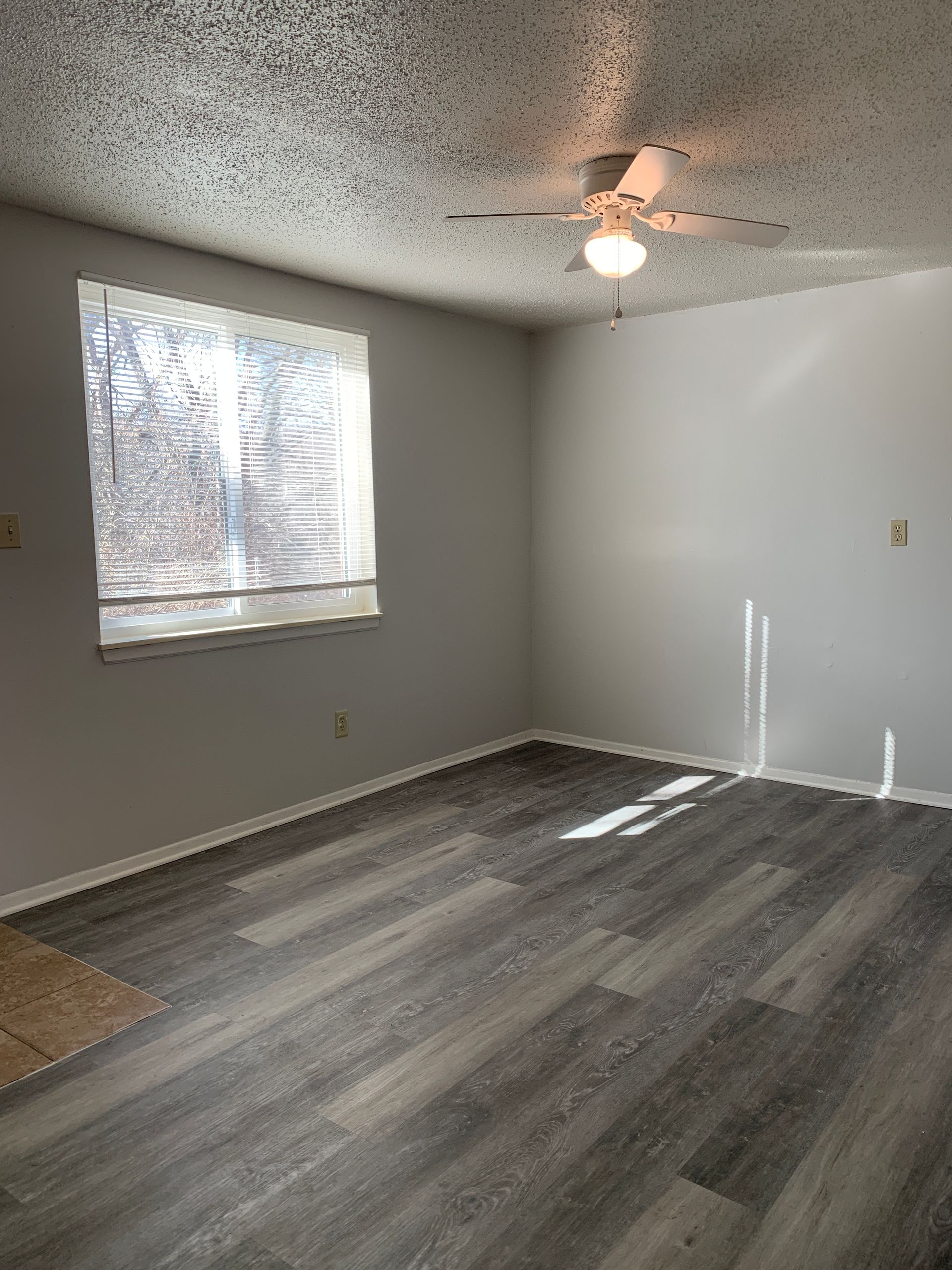 Empty room with gray laminate flooring, white walls, and a window with blinds.