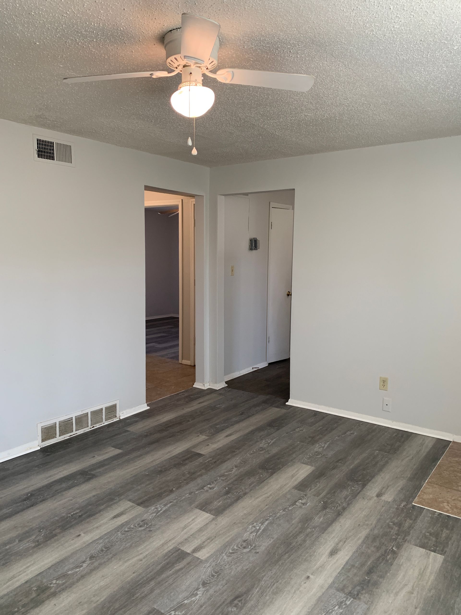 Living room with gray flooring, white walls, and a ceiling fan. Two doorways lead to other rooms.