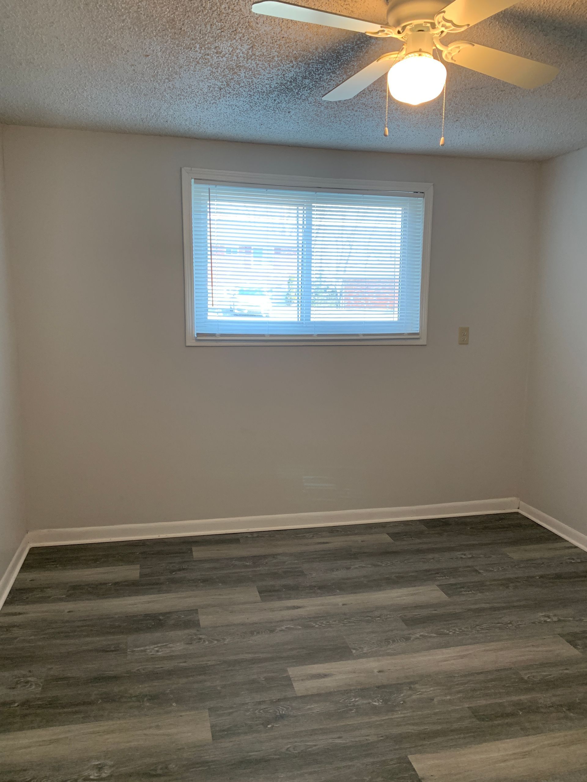 Empty room with a window, blinds, and a ceiling fan, gray-toned flooring, and white walls.