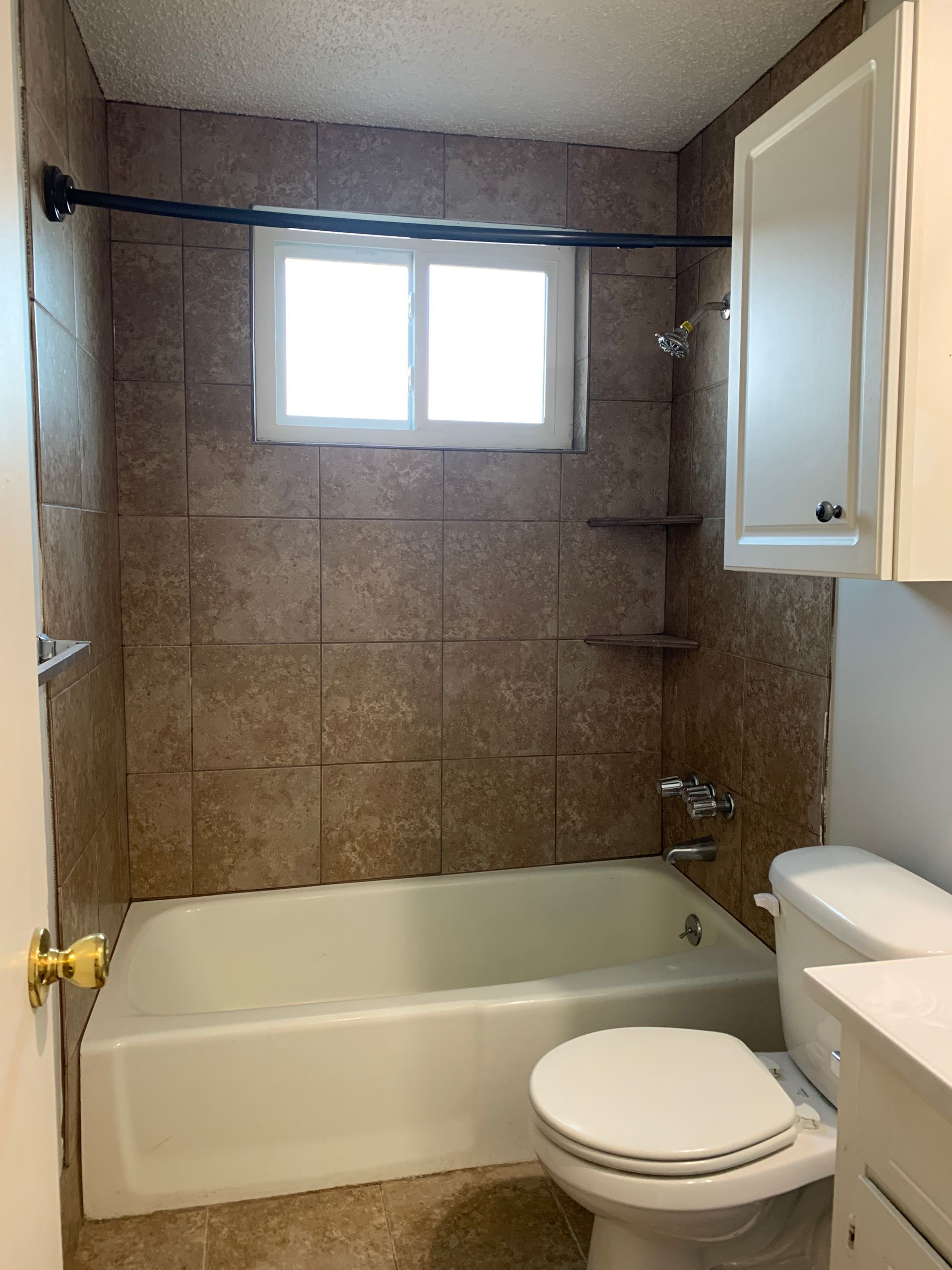 Bathroom with a white bathtub, toilet, and tiled walls. A small window is centered above the tub.