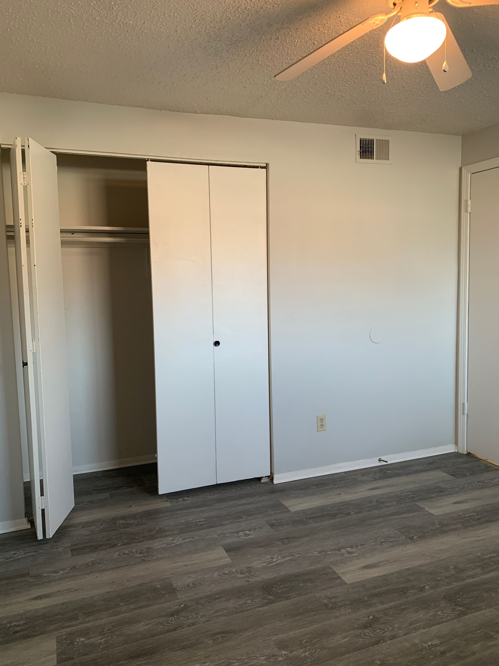 Bedroom interior with a closet and partially opened doors. Gray flooring, white walls, and a ceiling fan.