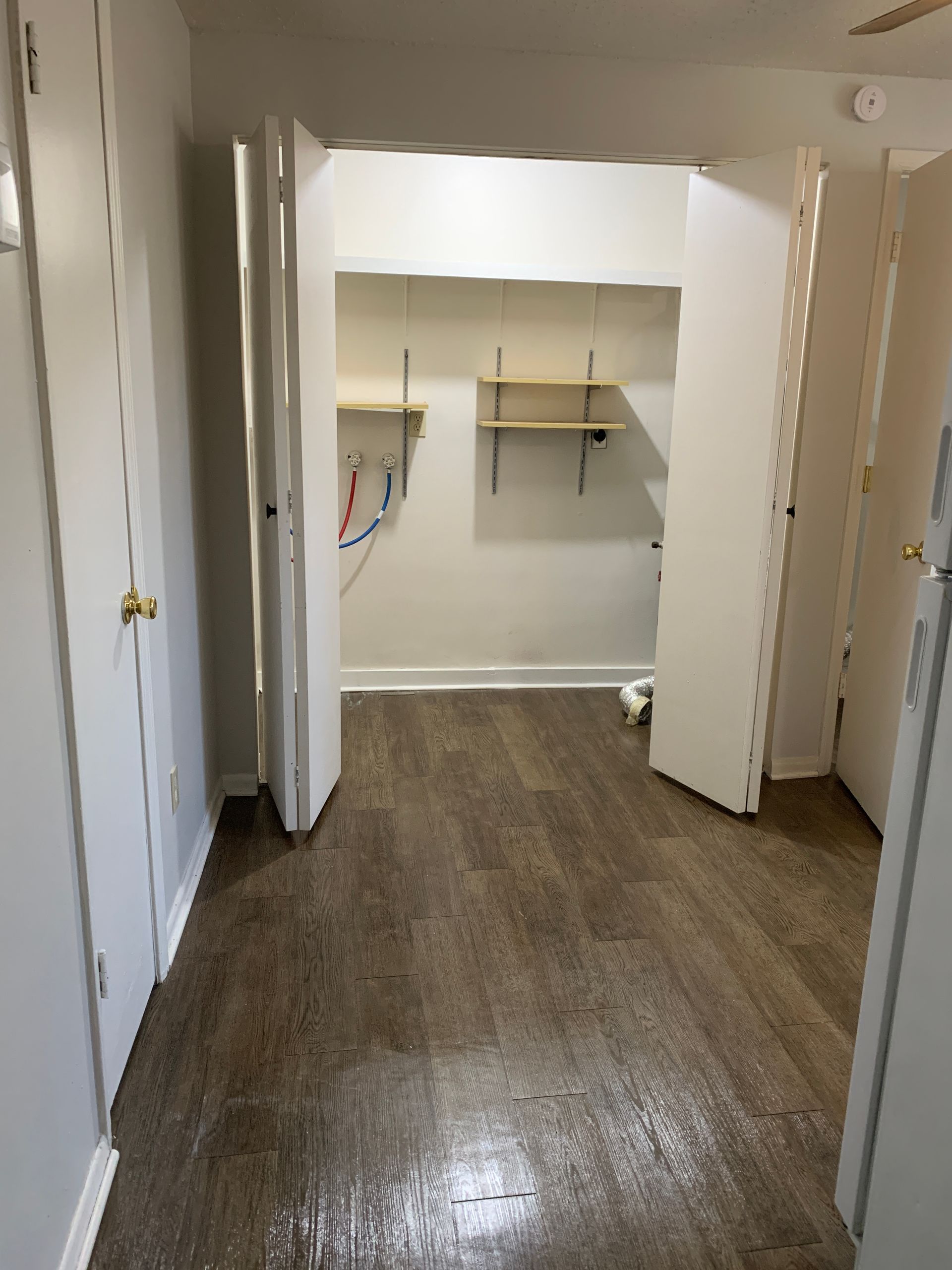 Narrow hallway with open closet, brown flooring, white doors and walls.