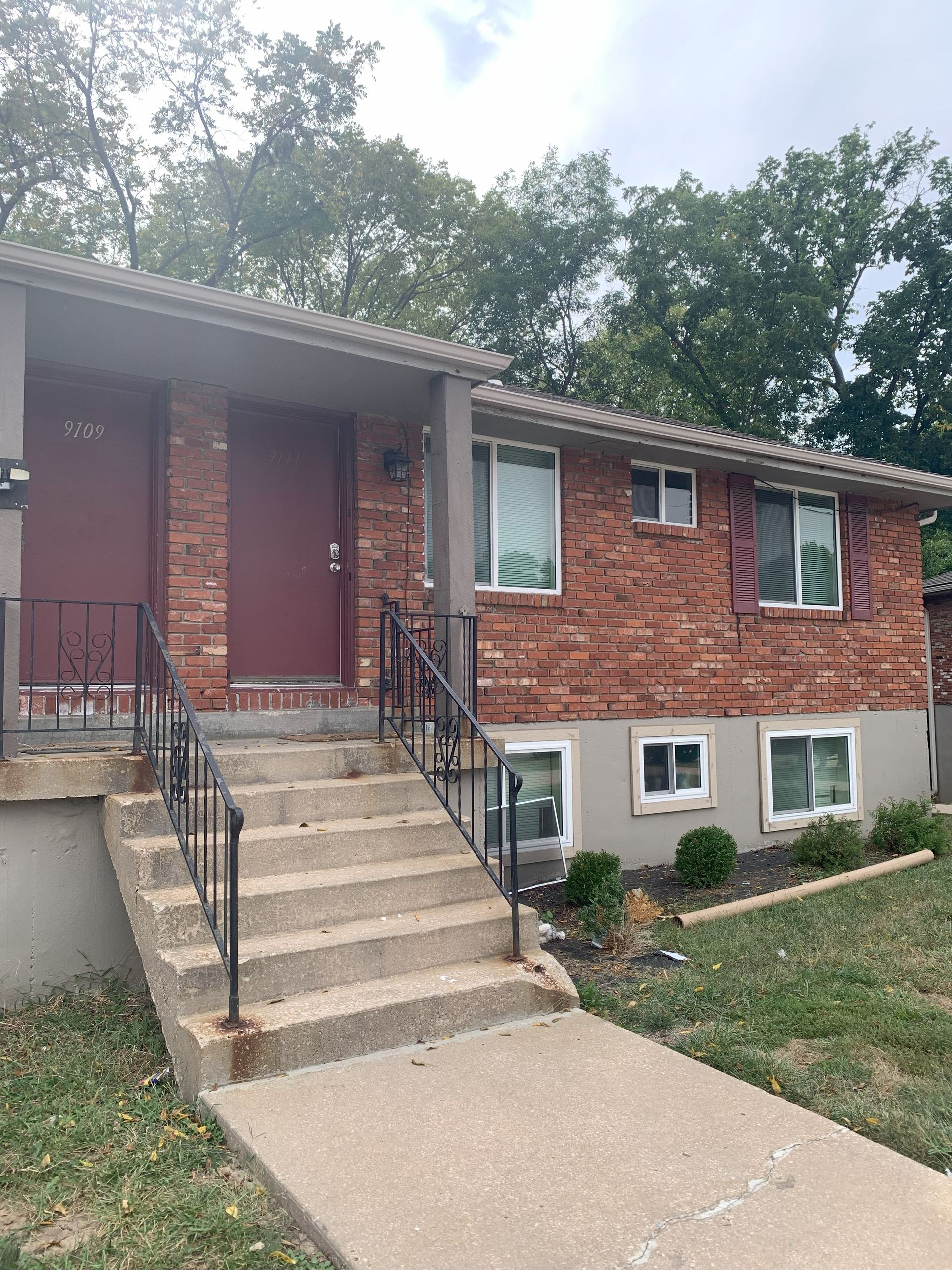 Brick apartment building with red doors, stairs, and green landscaping.