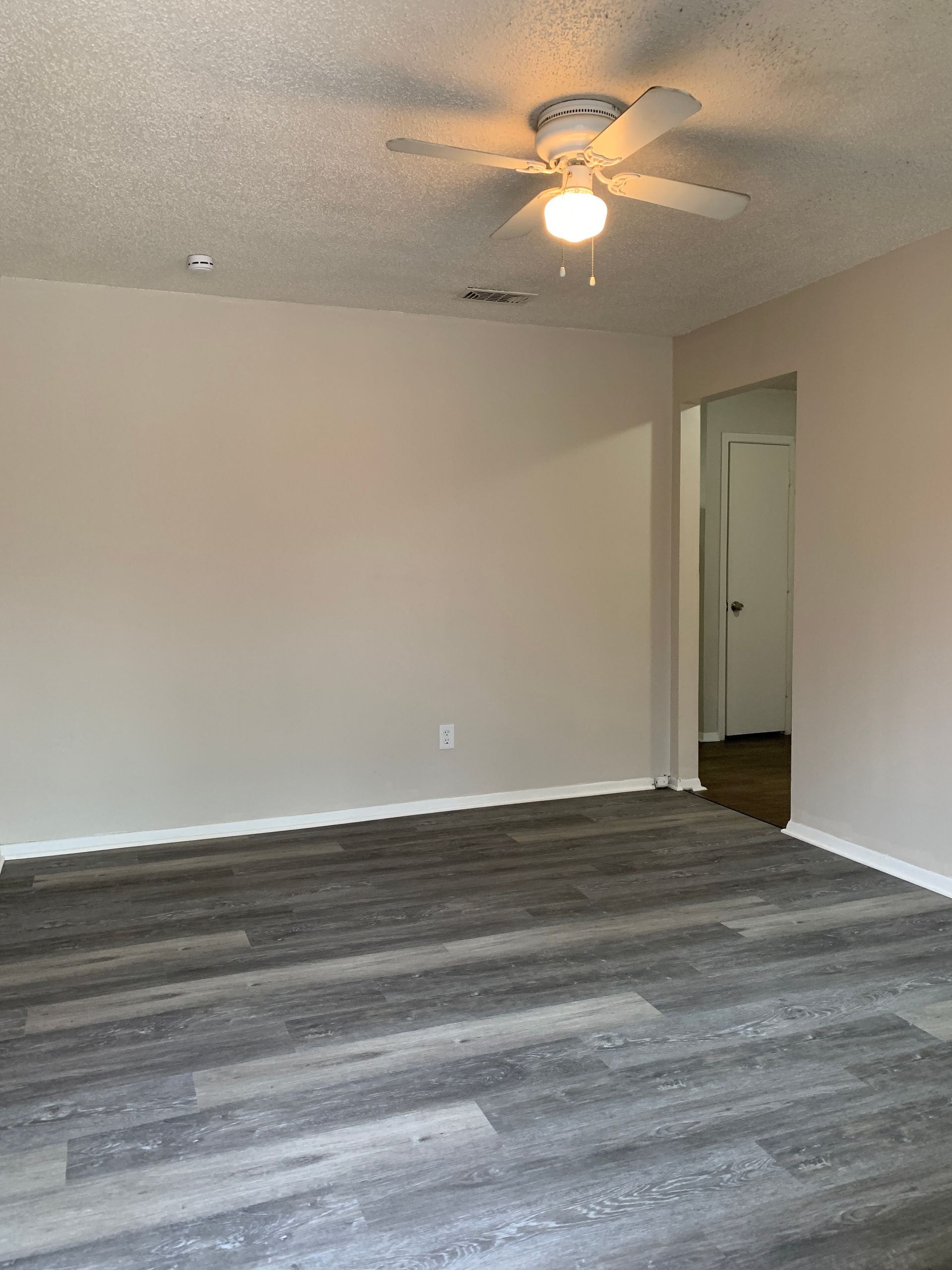 Empty room with gray wood-look flooring, beige walls, and a ceiling fan.
