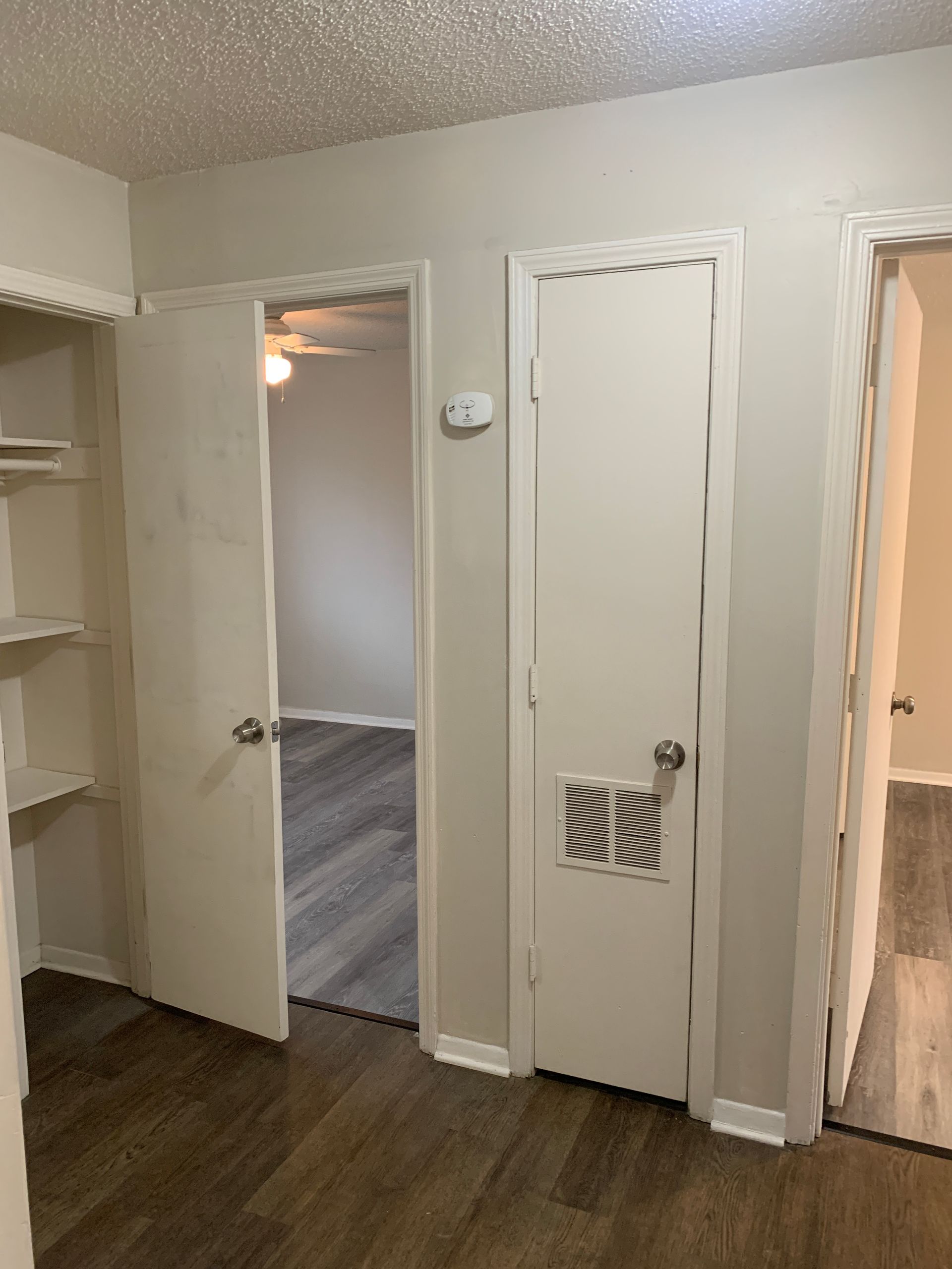 Hallway with three doorways, a bedroom, a closet, and a utility room.  Neutral colors and wood-look flooring.