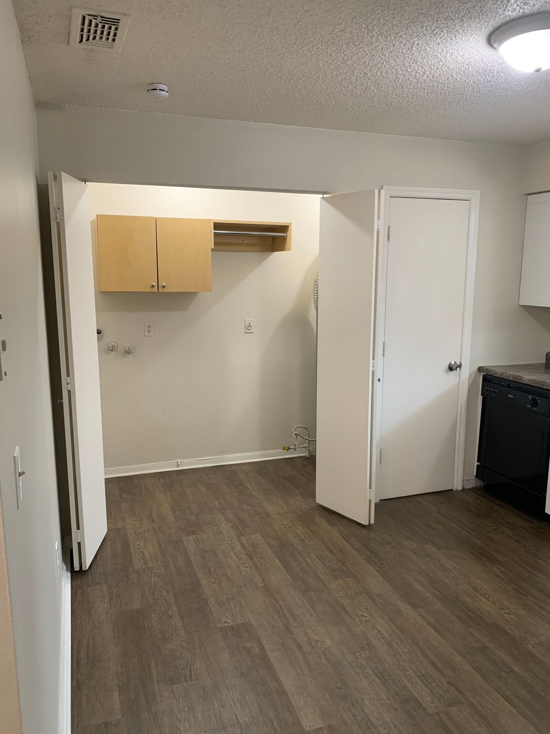 Empty kitchen area with wood-look flooring, white walls, and a laundry area.