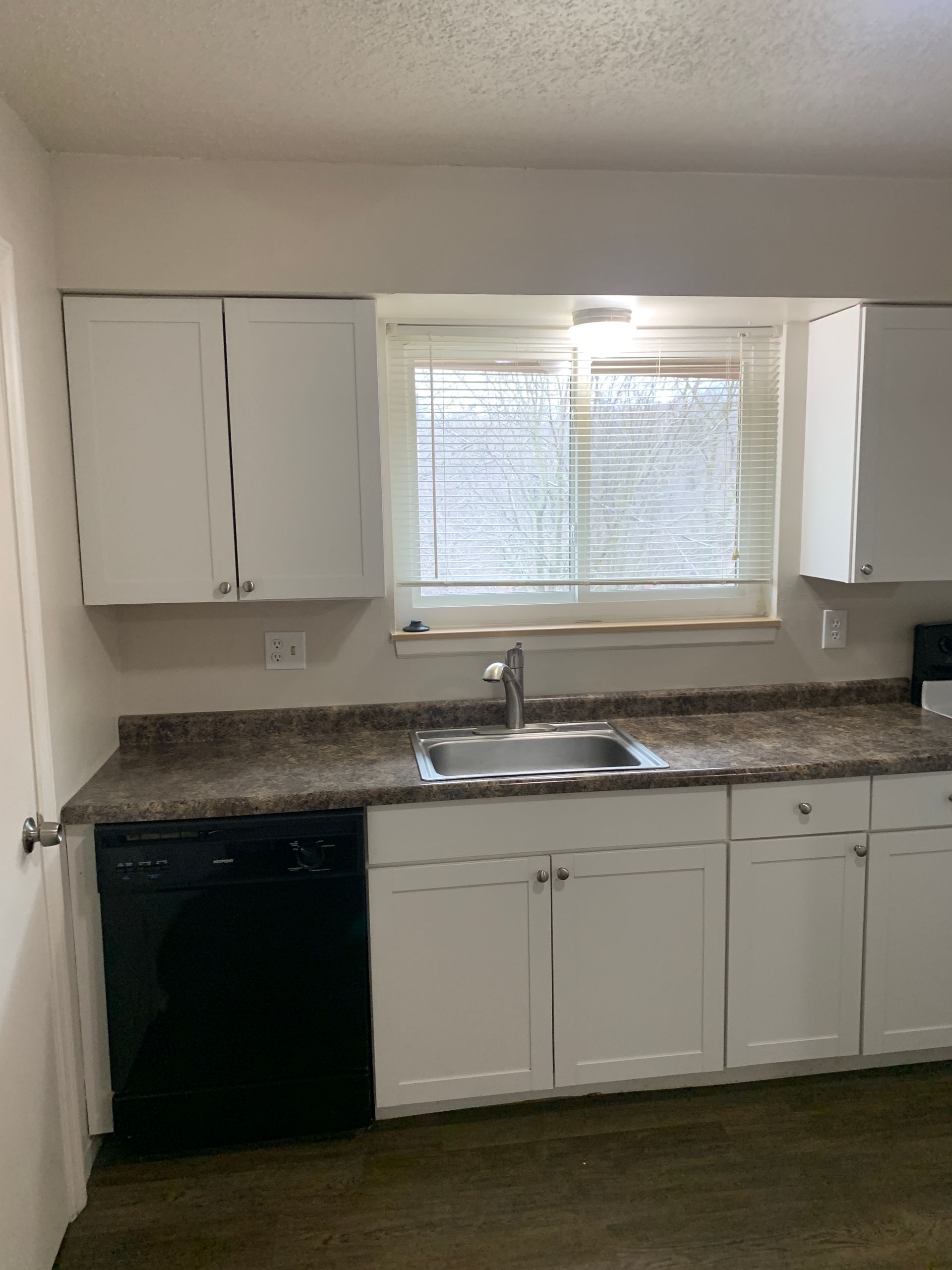 White kitchen cabinets with a black dishwasher and a window over the sink.