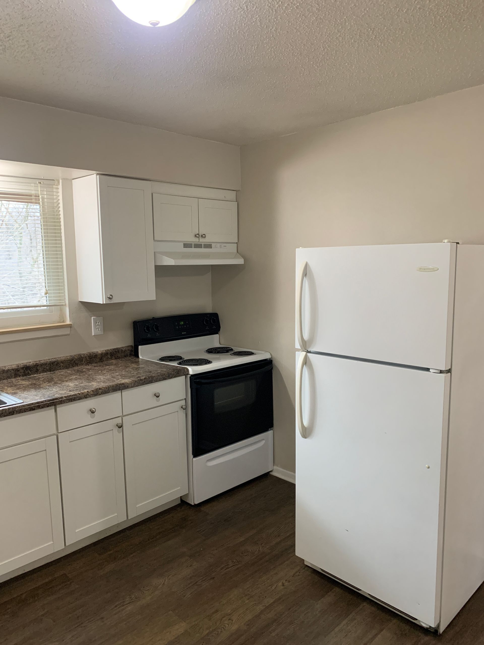 Kitchen with white cabinets, stove, and refrigerator. Brown countertop and light-colored walls.