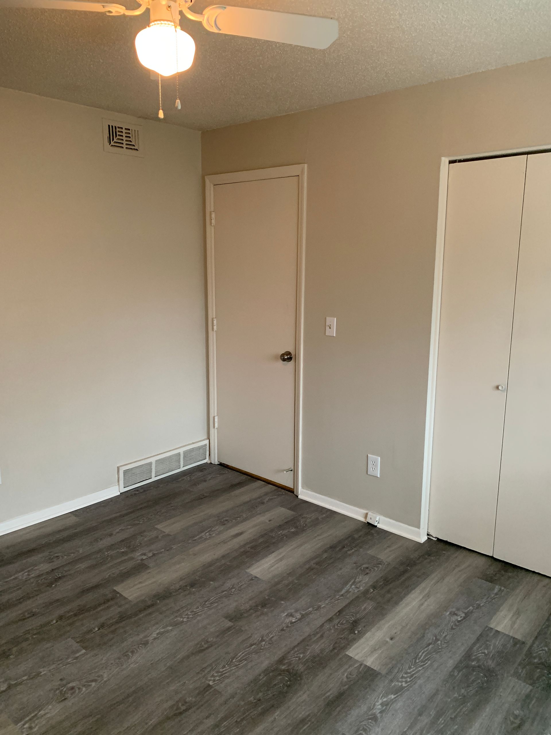 Empty bedroom with grey wood-look flooring, light grey walls, white doors, and a ceiling fan.