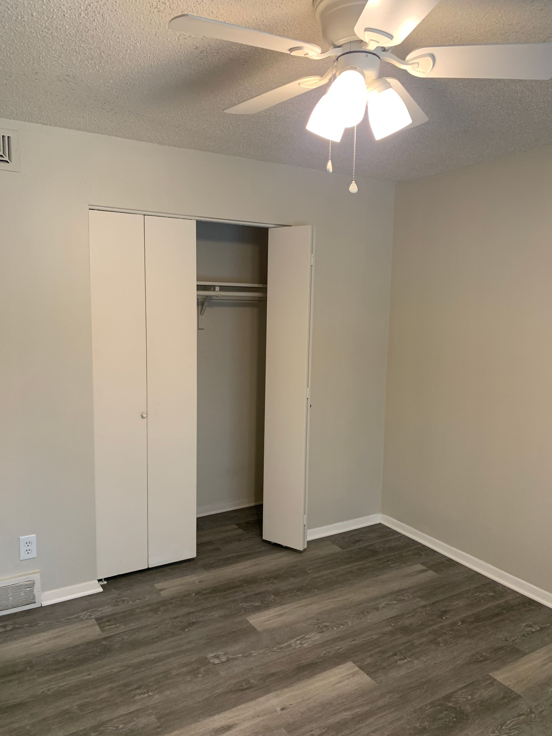 Bedroom with wood-look floor, light gray walls, white closet doors, and a ceiling fan.