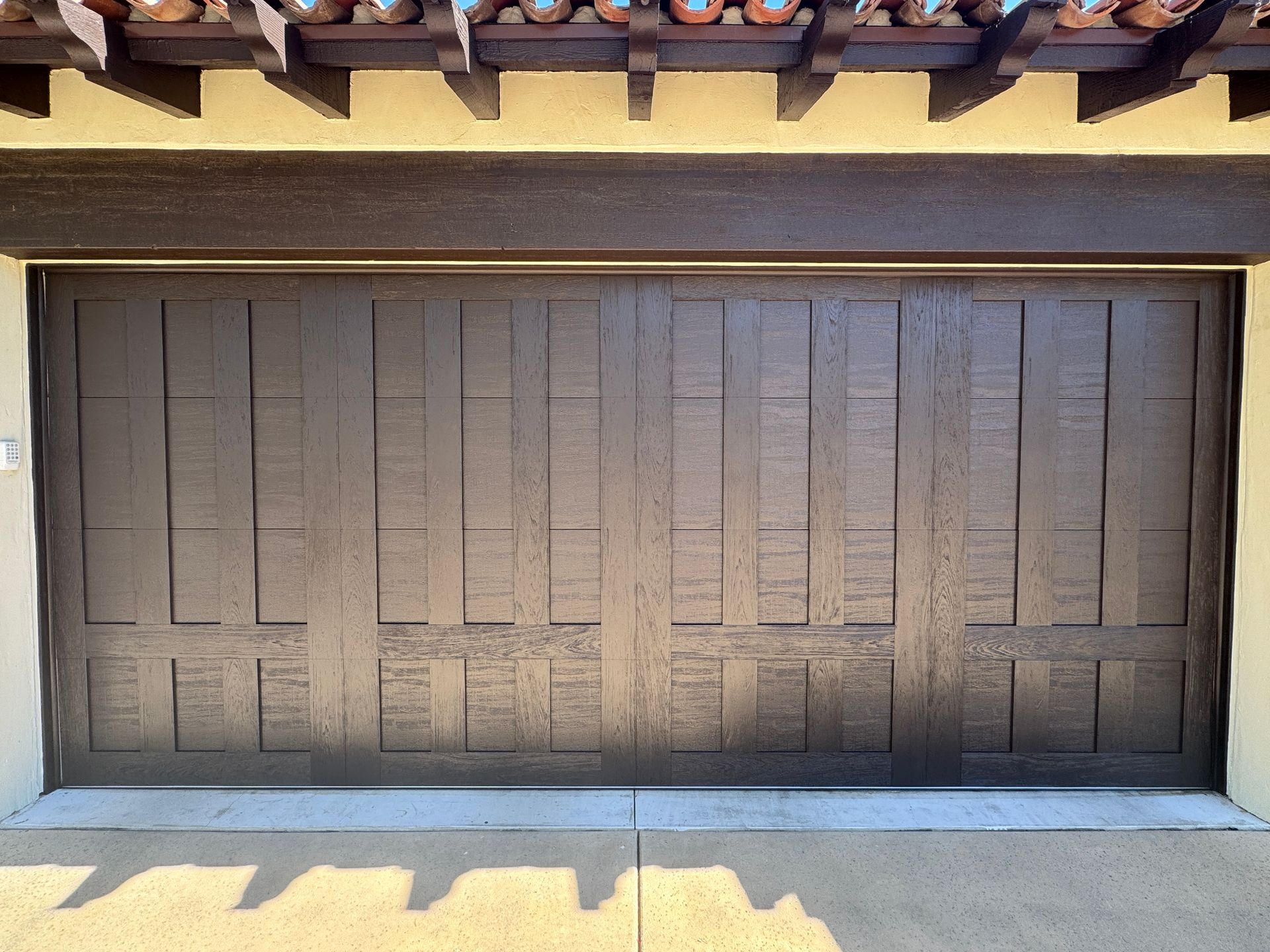 A dark brown, textured wooden garage door with a vertical paneled design, set beneath a pergola.