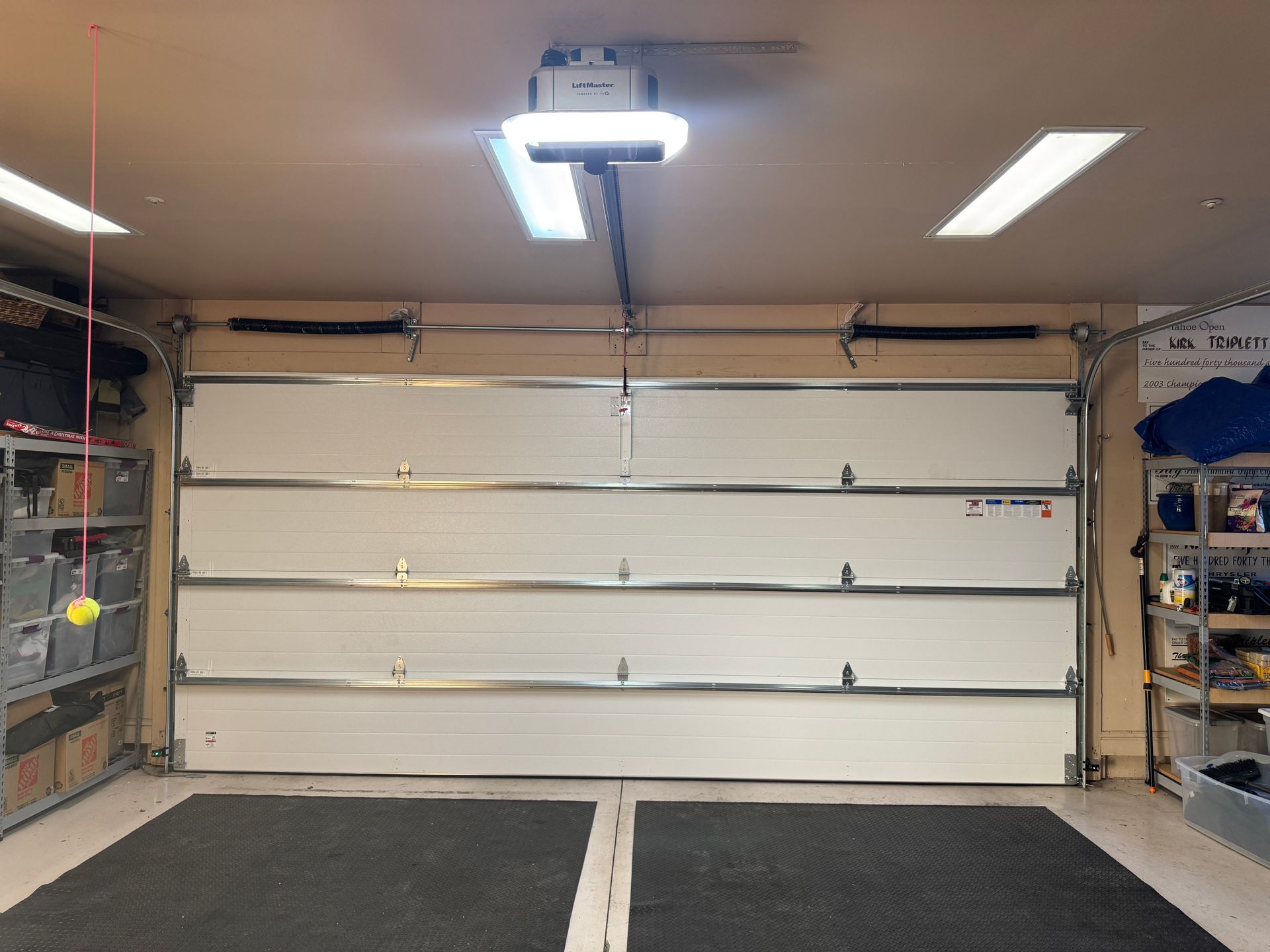 A closed white garage door with a central overhead motorized opener and metal storage shelving on either side.