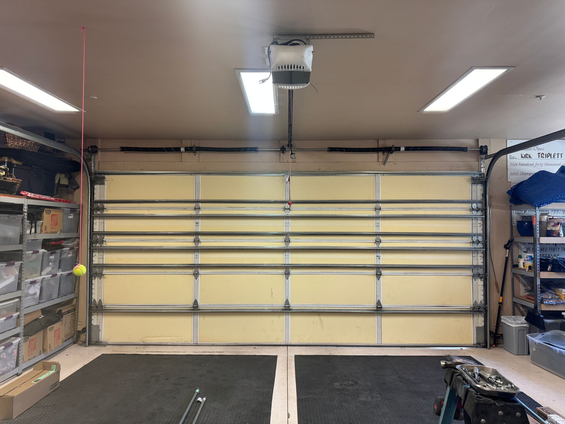 A closed garage door with an overhead motor, flanked by storage shelving in a residential garage.