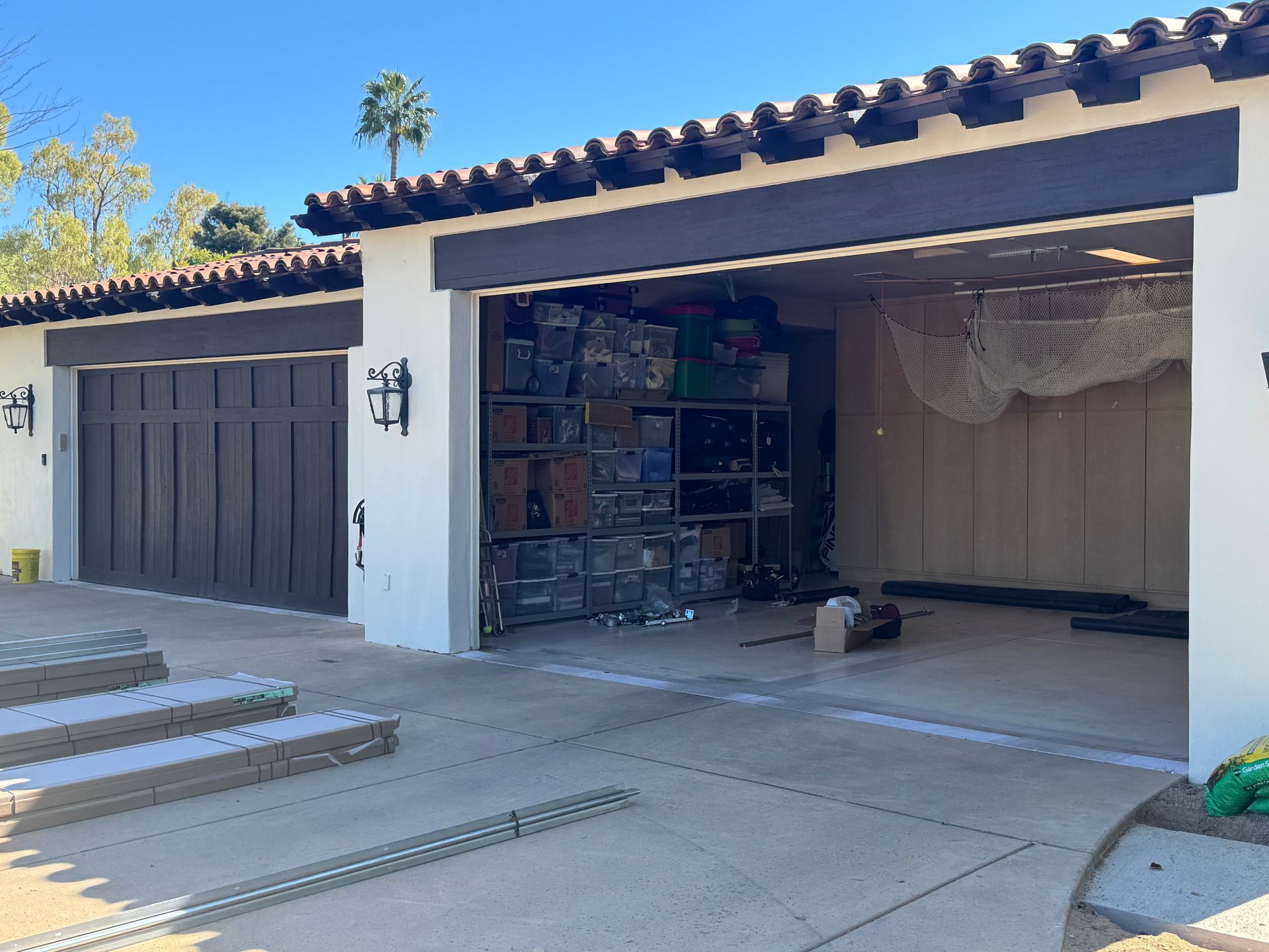 A two-car garage with one bay closed and the other open, revealing shelving units filled with boxes and storage items.