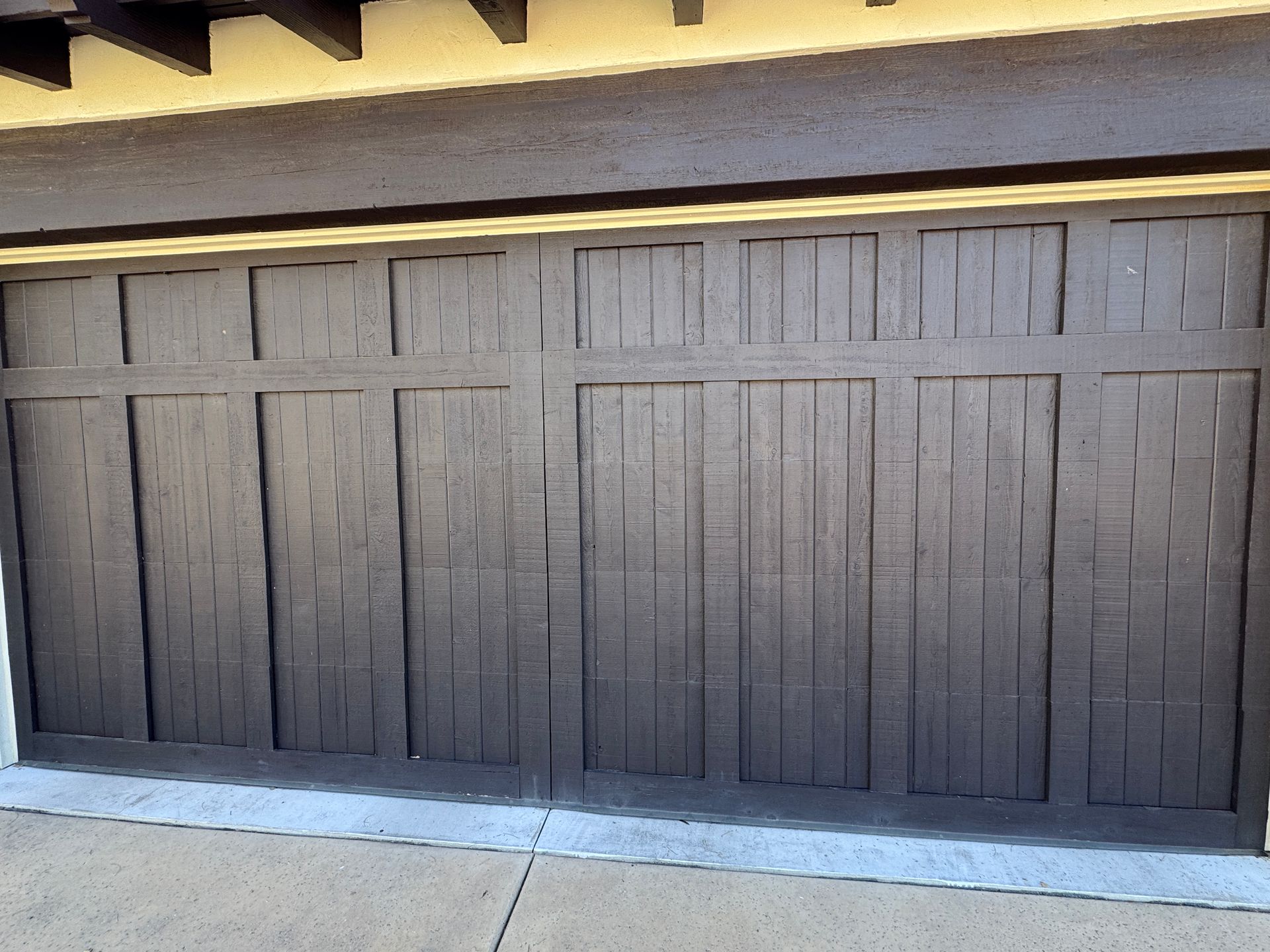 A dark brown garage door with a paneled design featuring vertical slats, viewed from an outdoor driveway.