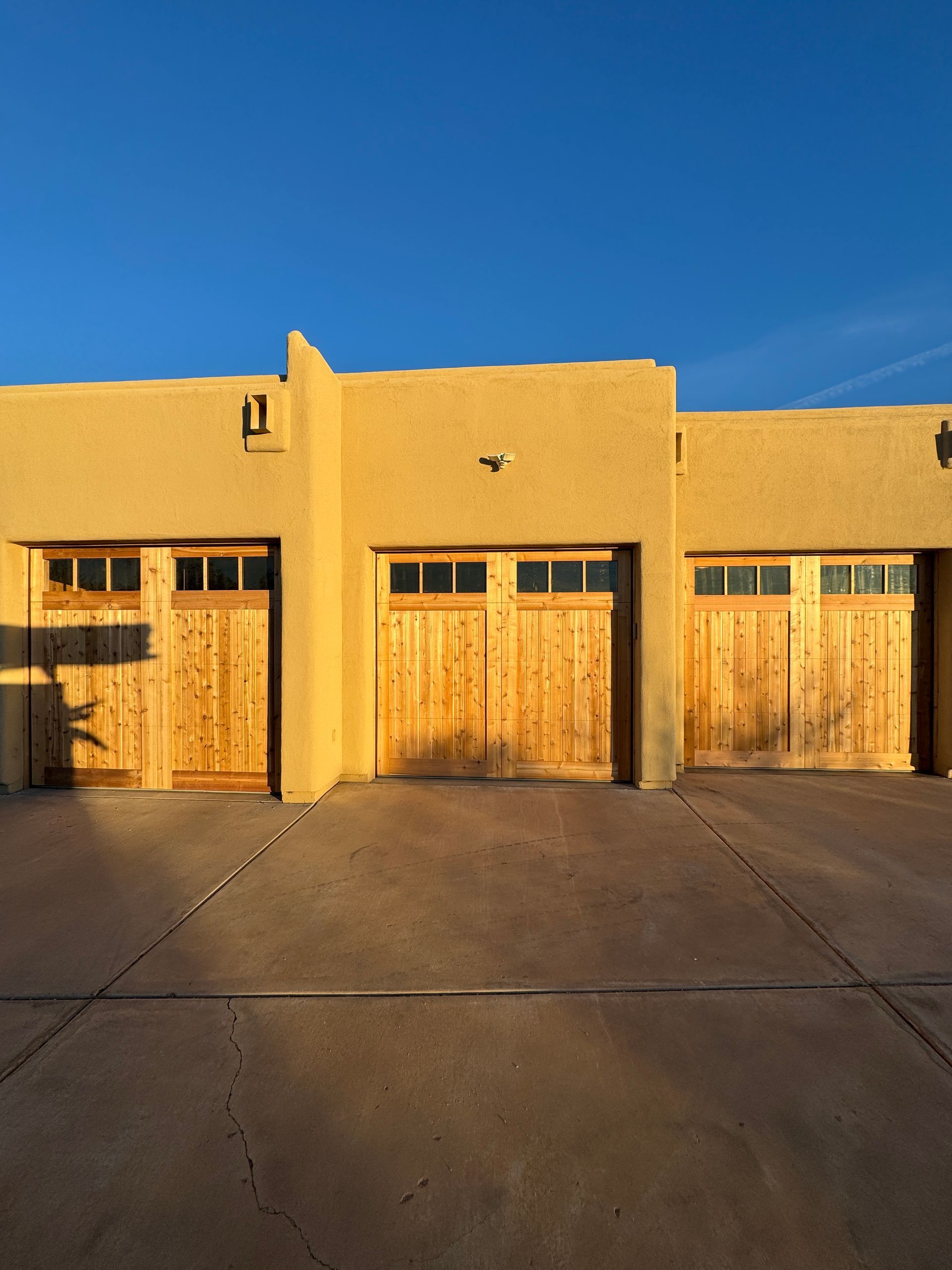 A tan, Southwest-style building with three wooden garage doors under a clear blue sky.