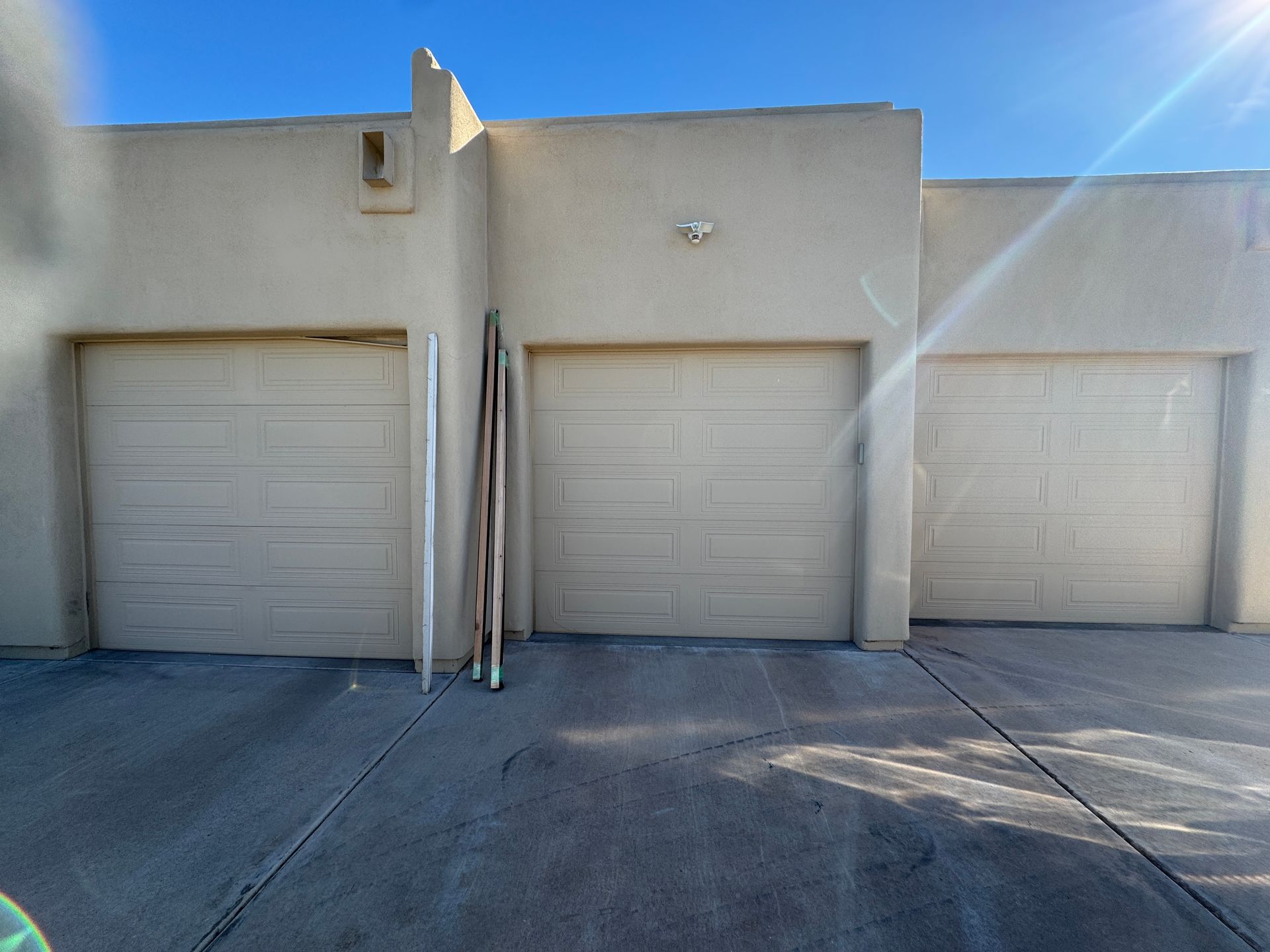 Three beige garage doors on a stucco building exterior under a bright, sunny sky.