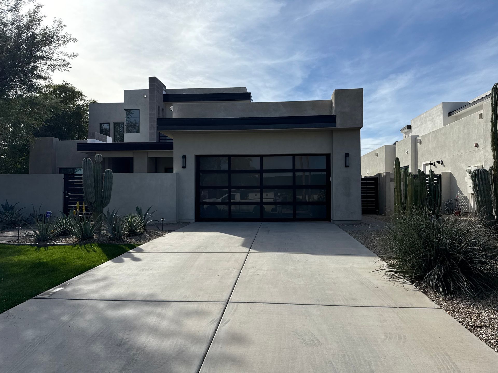 A modern, two-story beige house with a large black-framed glass garage door, fronted by a concrete driveway.
